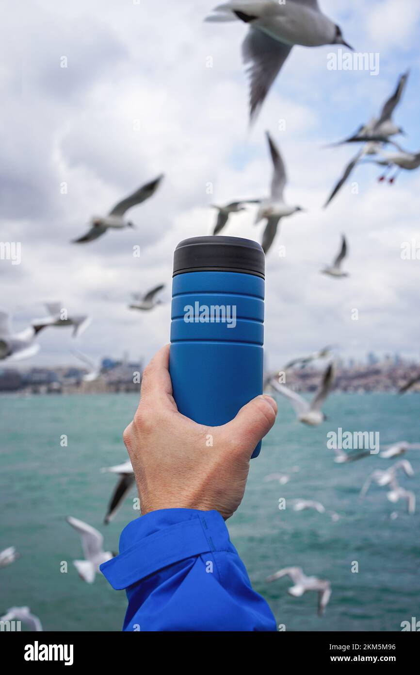 Nahaufnahme eines handgehaltenen Thermoreisetassens mit Möwen im Hintergrund. Stockfoto