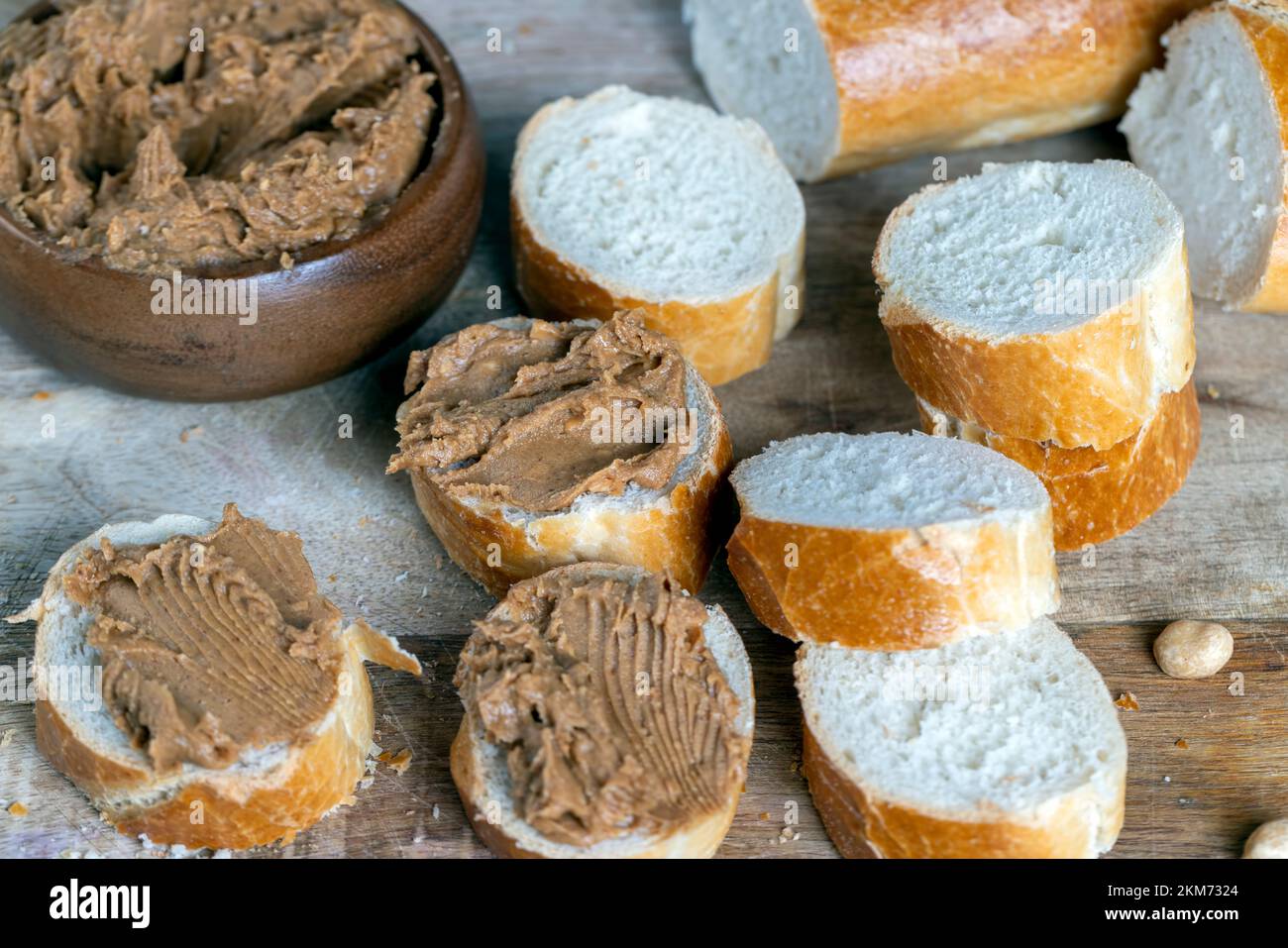 Erdnusspaste mit Stücken von Erdnüssen und weißem Baguette ...