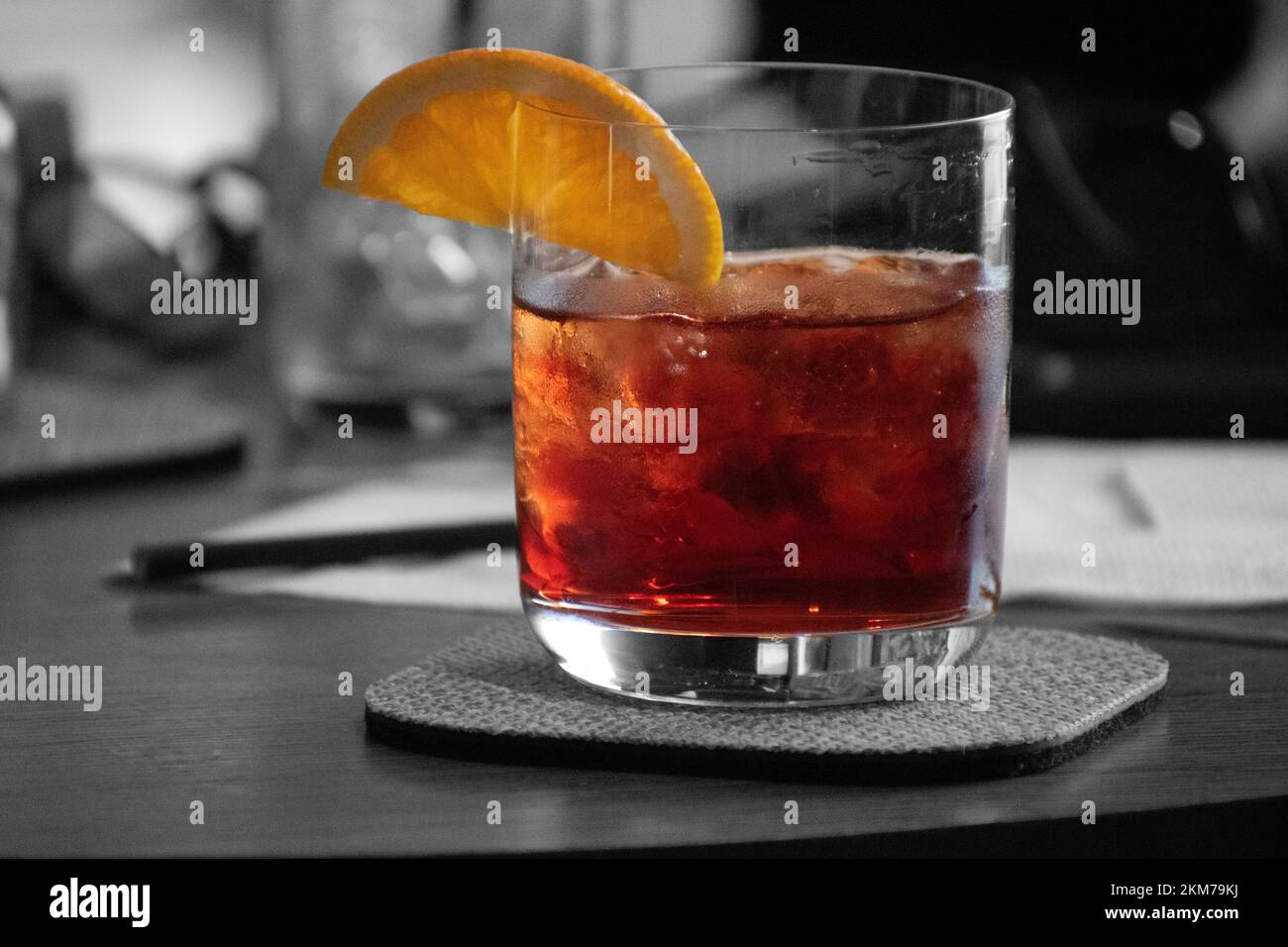 Farbenfroher roter Cocktail auf Eis mit einem Stück Orange am Glasrand. Stockfoto