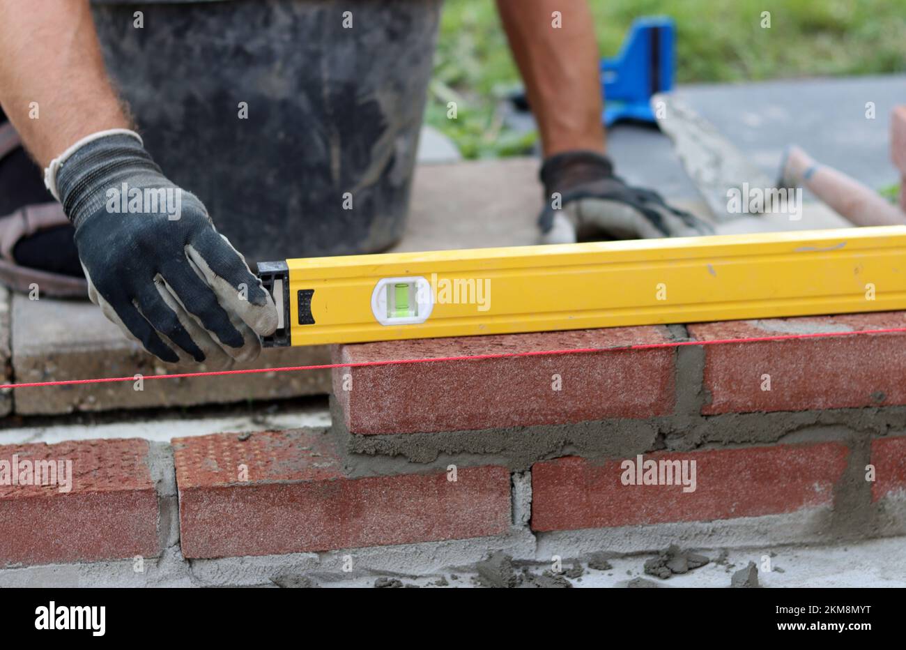 Bauarbeiten im Gange. Männlicher Baumeister, der mit roten Ziegeln arbeitet. Nahaufnahme der Mauerwand. Stockfoto