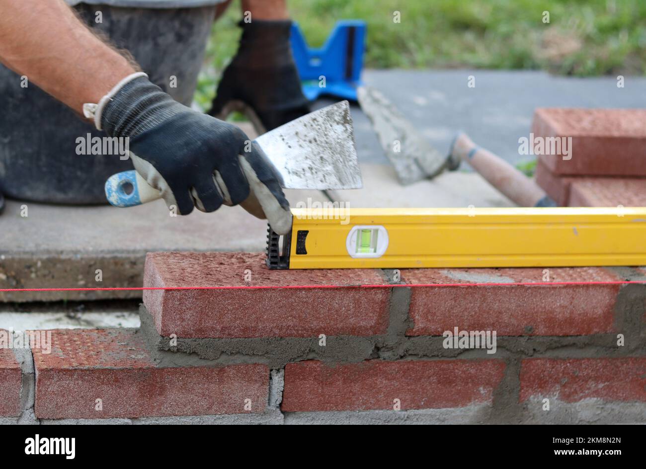 Bauarbeiten im Gange. Männlicher Baumeister, der mit roten Ziegeln arbeitet. Nahaufnahme der Mauerwand. Stockfoto