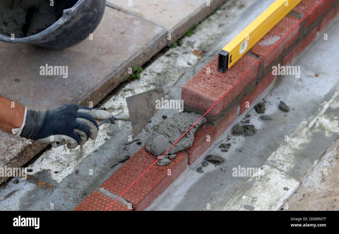 Bauarbeiten im Gange. Männlicher Baumeister, der mit roten Ziegeln arbeitet. Nahaufnahme der Mauerwand. Stockfoto