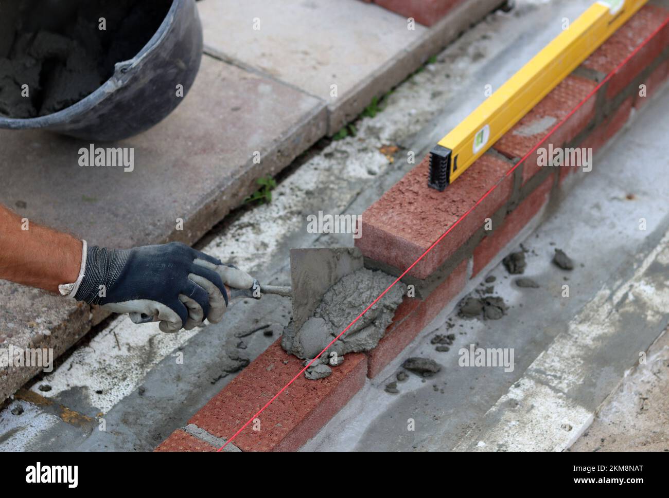 Bauarbeiten im Gange. Männlicher Baumeister, der mit roten Ziegeln arbeitet. Nahaufnahme der Mauerwand. Stockfoto