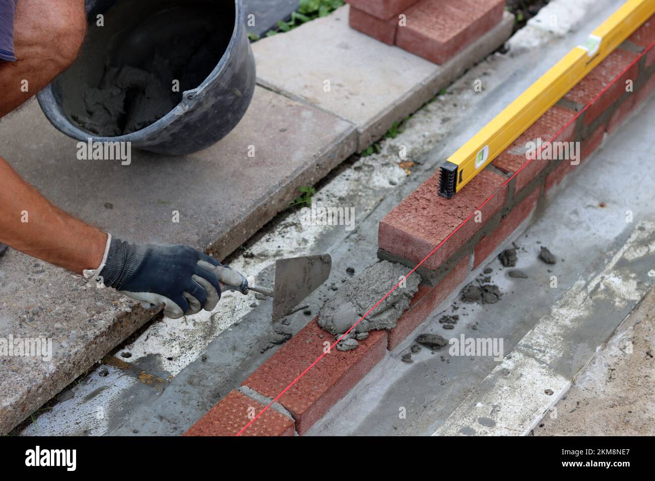 Bauarbeiten im Gange. Männlicher Baumeister, der mit roten Ziegeln arbeitet. Nahaufnahme der Mauerwand. Stockfoto