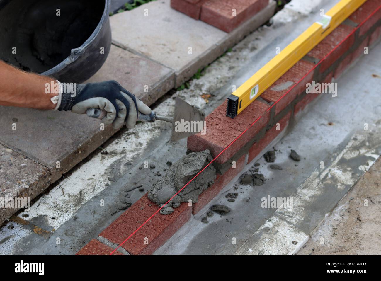 Bauarbeiten im Gange. Männlicher Baumeister, der mit roten Ziegeln arbeitet. Nahaufnahme der Mauerwand. Stockfoto