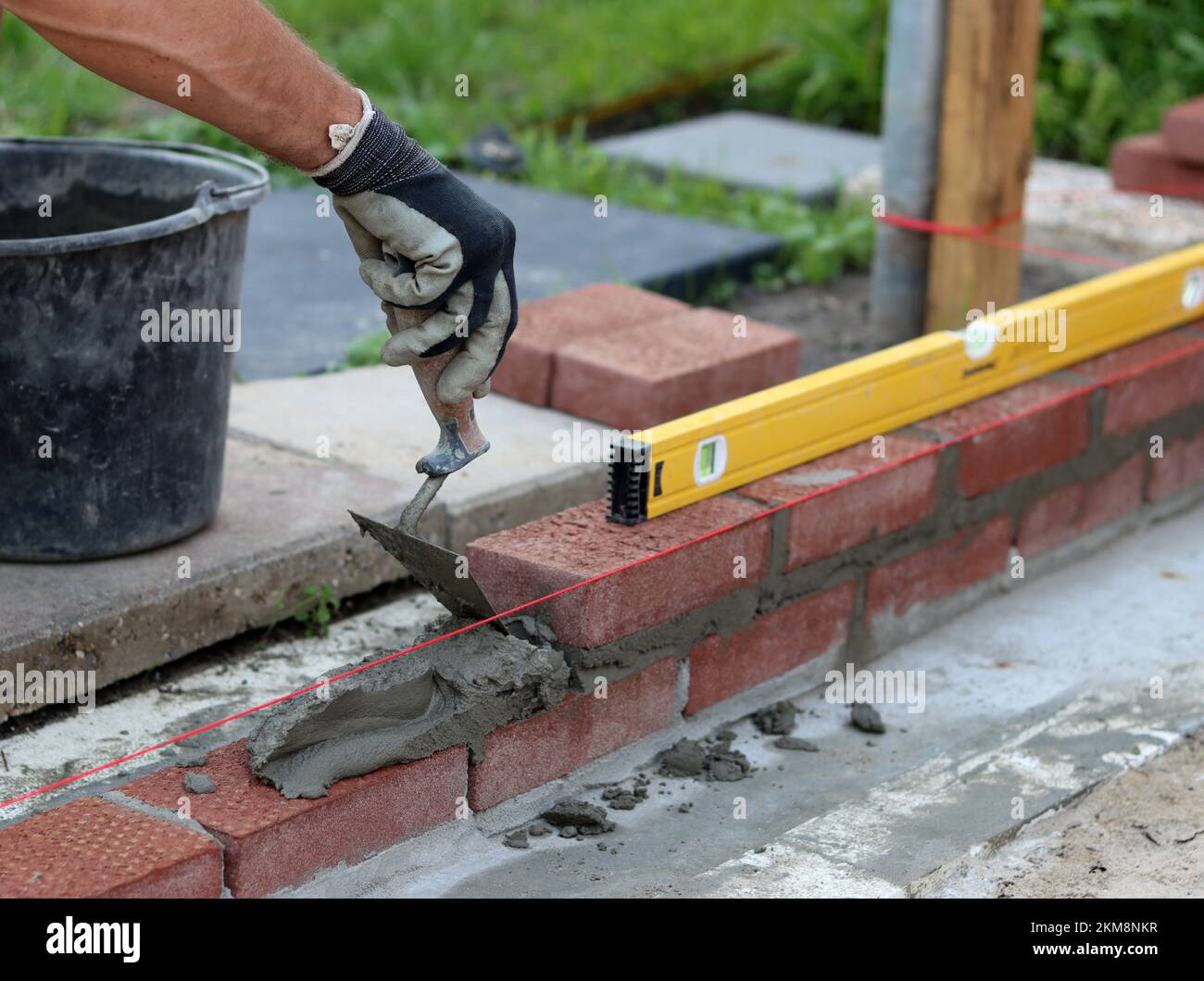 Bauarbeiten im Gange. Männlicher Baumeister, der mit roten Ziegeln arbeitet. Nahaufnahme der Mauerwand. Stockfoto