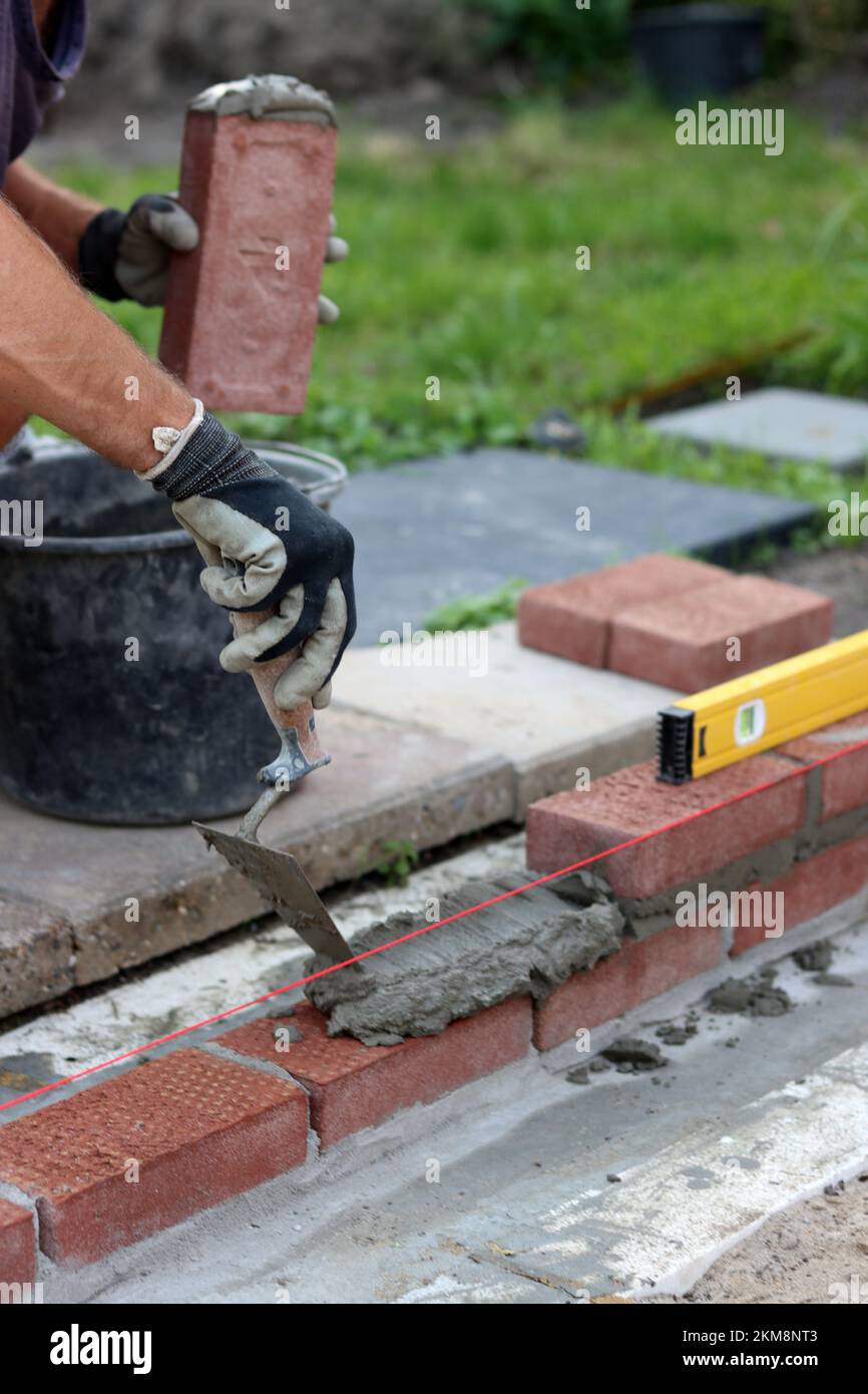 Bauarbeiten im Gange. Männlicher Baumeister, der mit roten Ziegeln arbeitet. Nahaufnahme der Mauerwand. Stockfoto