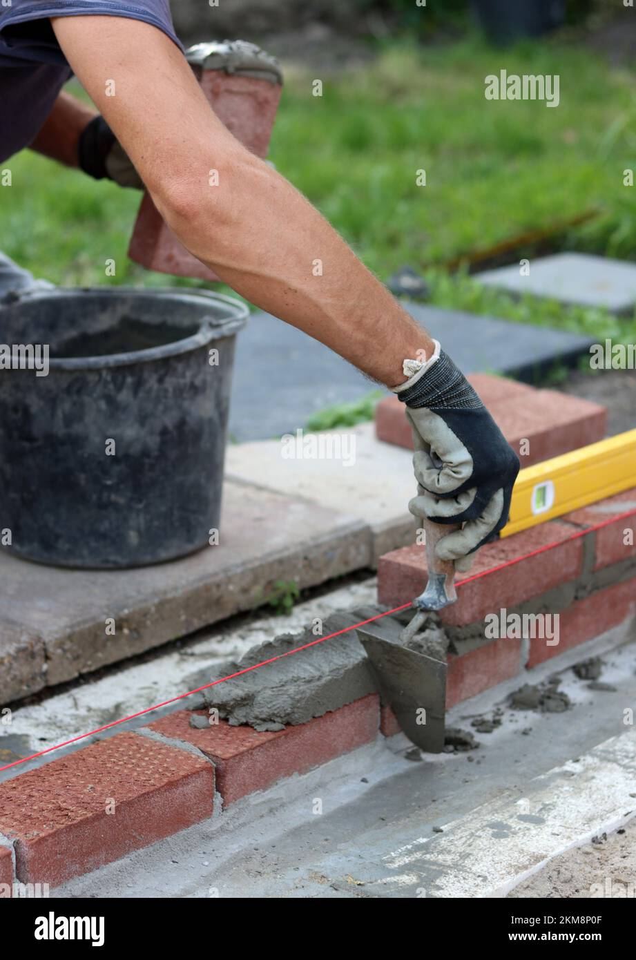 Bauarbeiten im Gange. Männlicher Baumeister, der mit roten Ziegeln arbeitet. Nahaufnahme der Mauerwand. Stockfoto