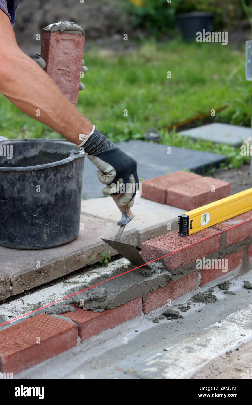 Bauarbeiten im Gange. Männlicher Baumeister, der mit roten Ziegeln arbeitet. Nahaufnahme der Mauerwand. Stockfoto