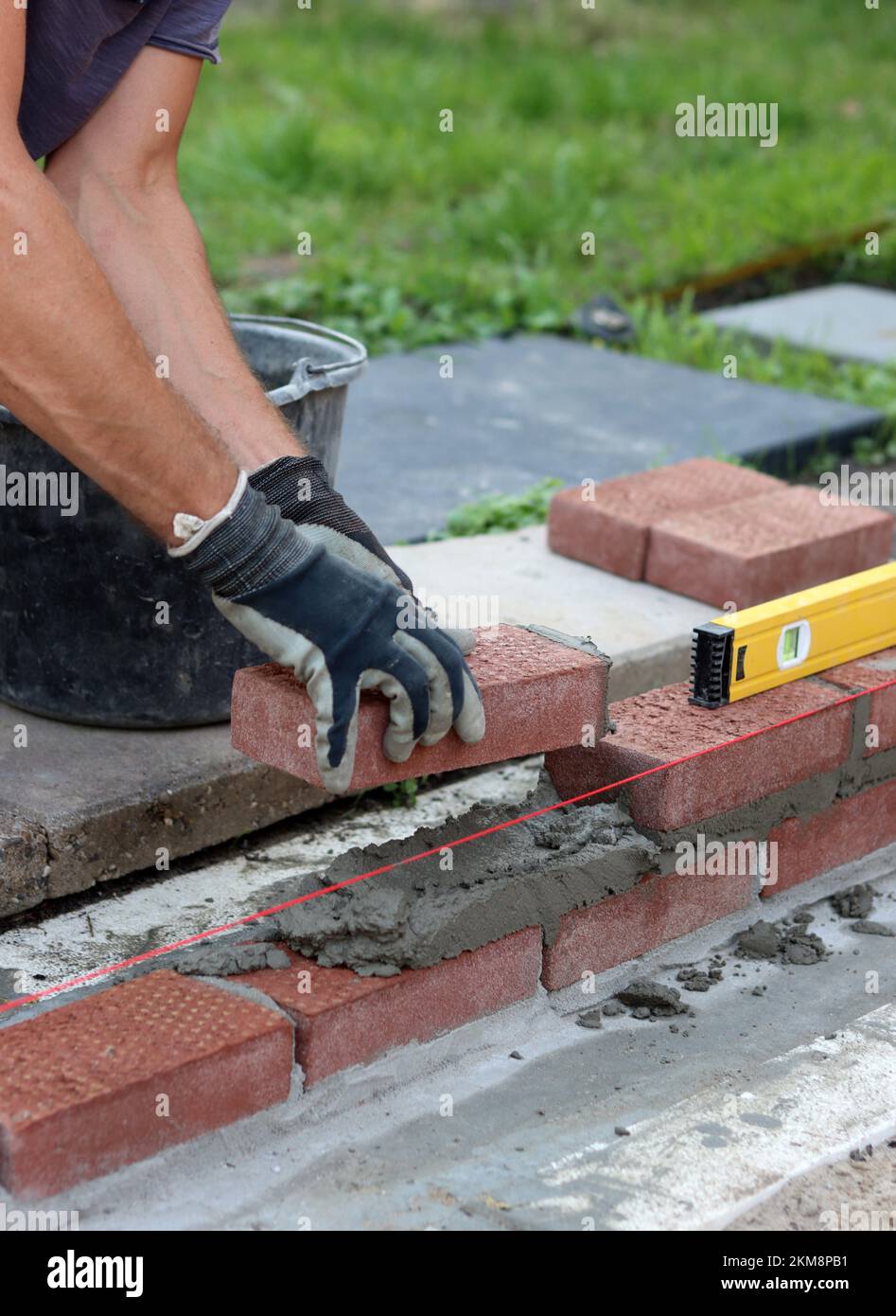 Nahaufnahme von männlichen Händen mit rotem Ziegel. Baustellenkonzept. Professioneller Bau einer Ziegelwand. Stockfoto