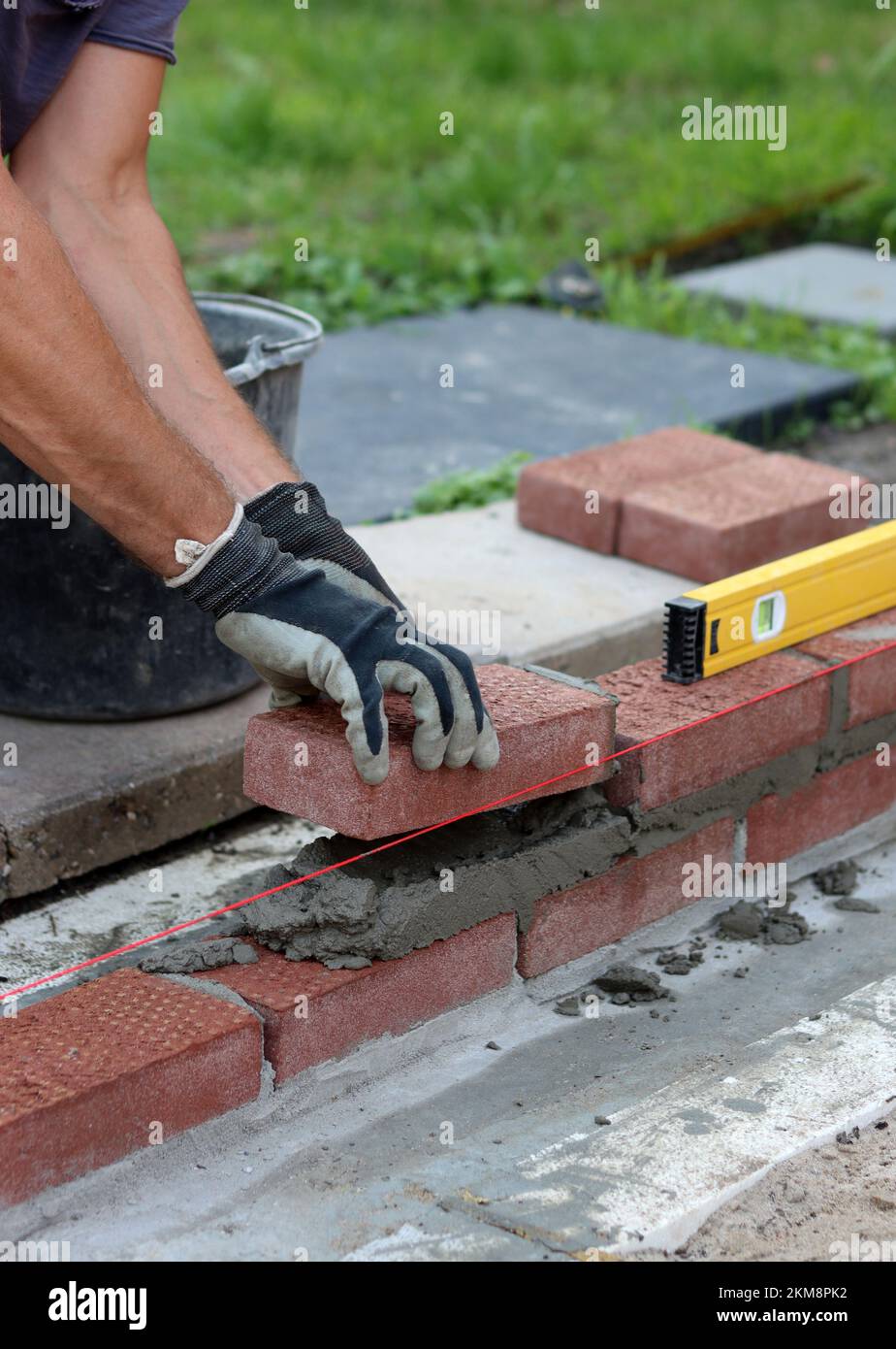 Nahaufnahme von männlichen Händen mit rotem Ziegel. Baustellenkonzept. Professioneller Bau einer Ziegelwand. Stockfoto