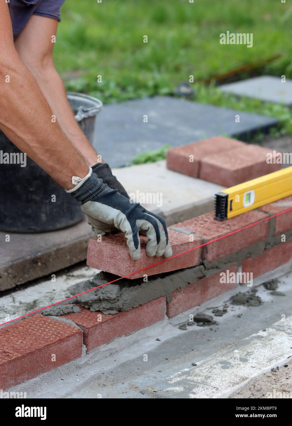 Nahaufnahme von männlichen Händen mit rotem Ziegel. Baustellenkonzept. Professioneller Bau einer Ziegelwand. Stockfoto