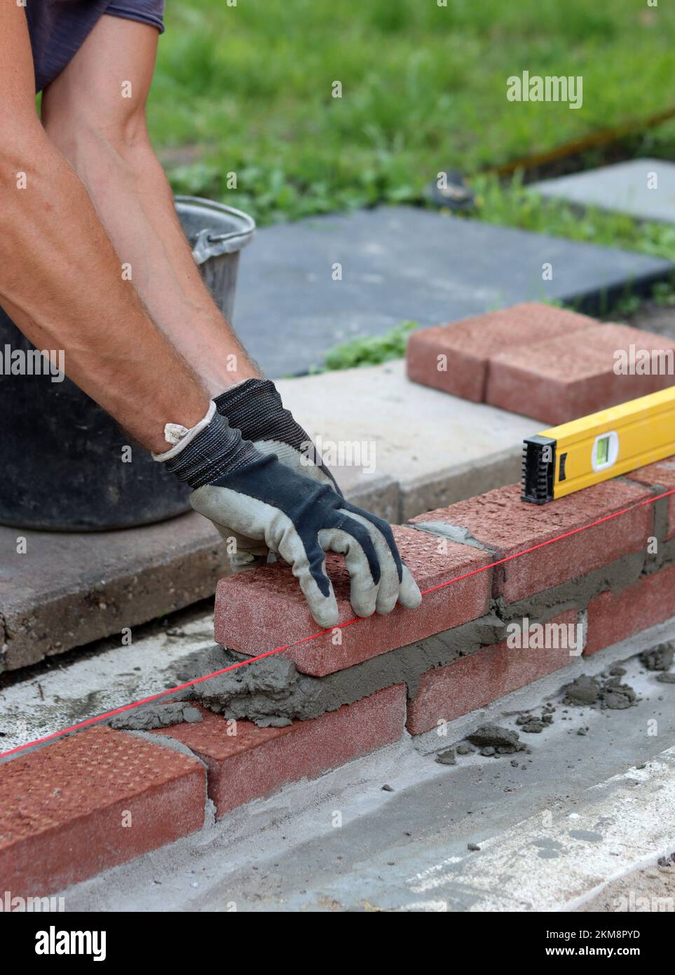 Nahaufnahme von männlichen Händen mit rotem Ziegel. Baustellenkonzept. Professioneller Bau einer Ziegelwand. Stockfoto