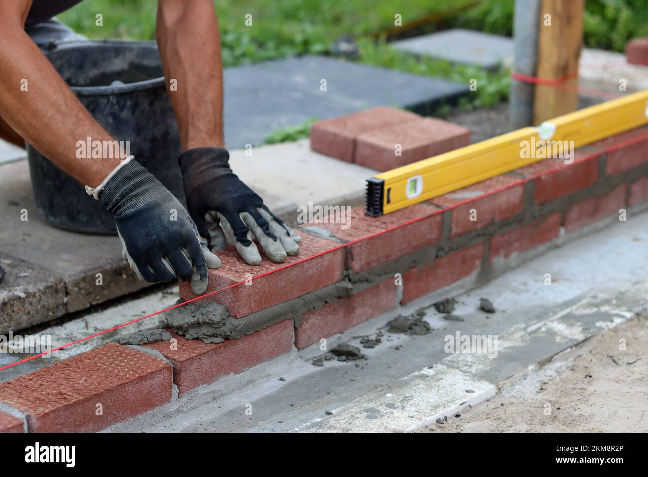 Bauarbeiten im Gange. Männlicher Baumeister, der mit roten Ziegeln arbeitet. Nahaufnahme der Mauerwand. Stockfoto
