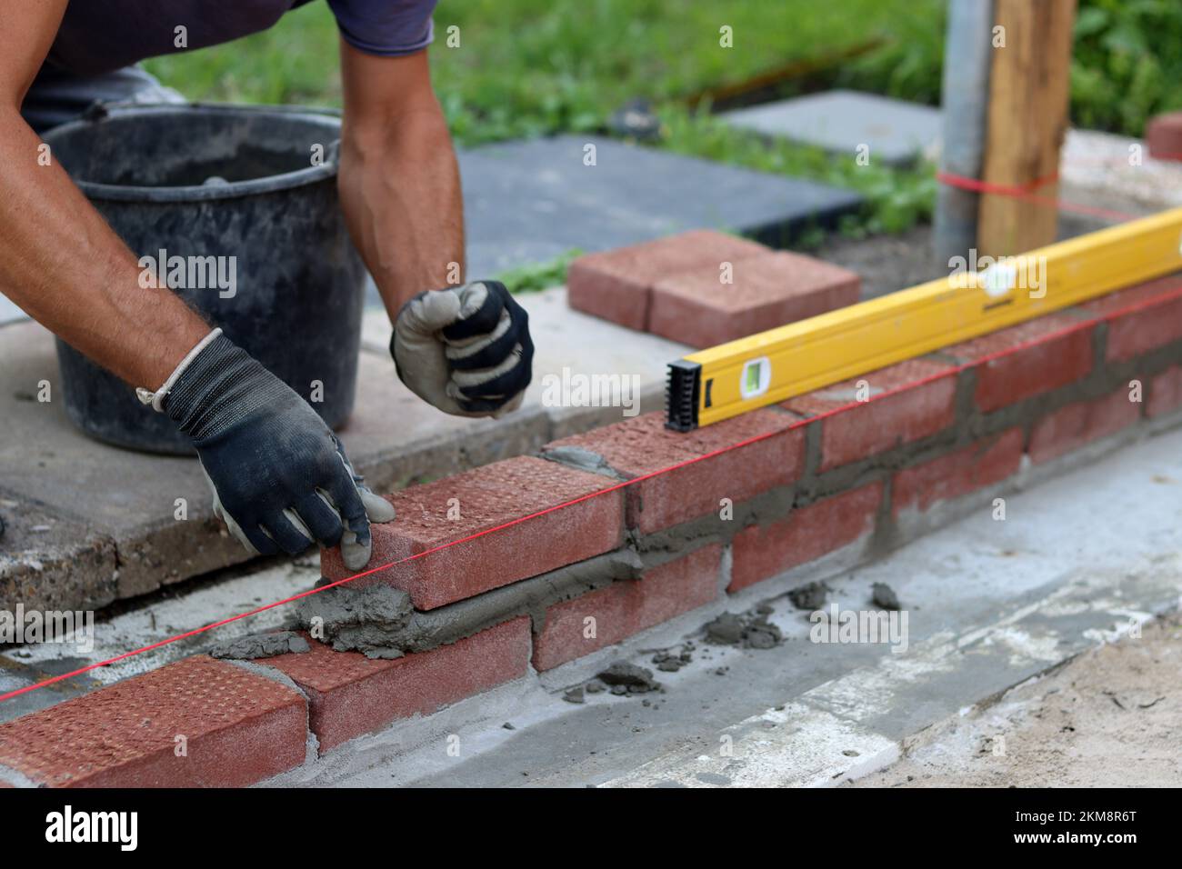 Nahaufnahme von männlichen Händen mit rotem Ziegel. Baustellenkonzept. Professioneller Bau einer Ziegelwand. Stockfoto