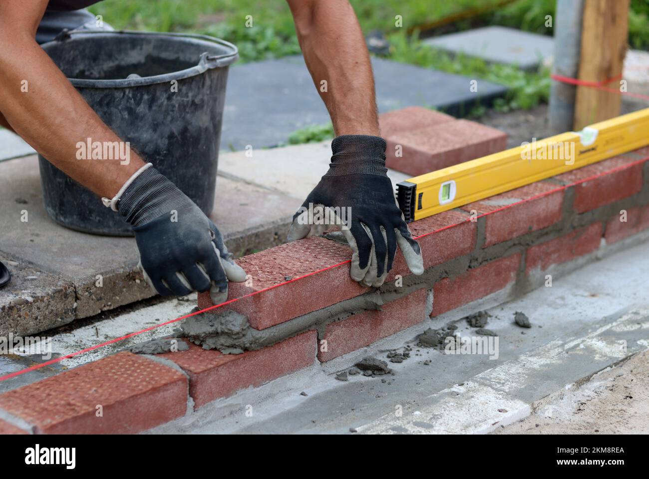 Nahaufnahme von männlichen Händen mit rotem Ziegel. Baustellenkonzept. Professioneller Bau einer Ziegelwand. Stockfoto