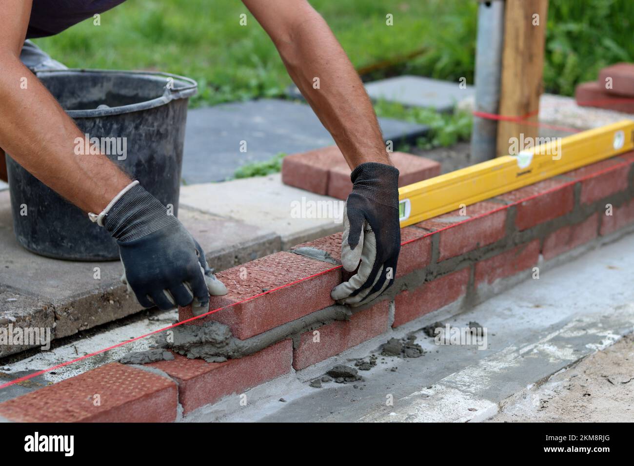Nahaufnahme von männlichen Händen mit rotem Ziegel. Baustellenkonzept. Professioneller Bau einer Ziegelwand. Stockfoto