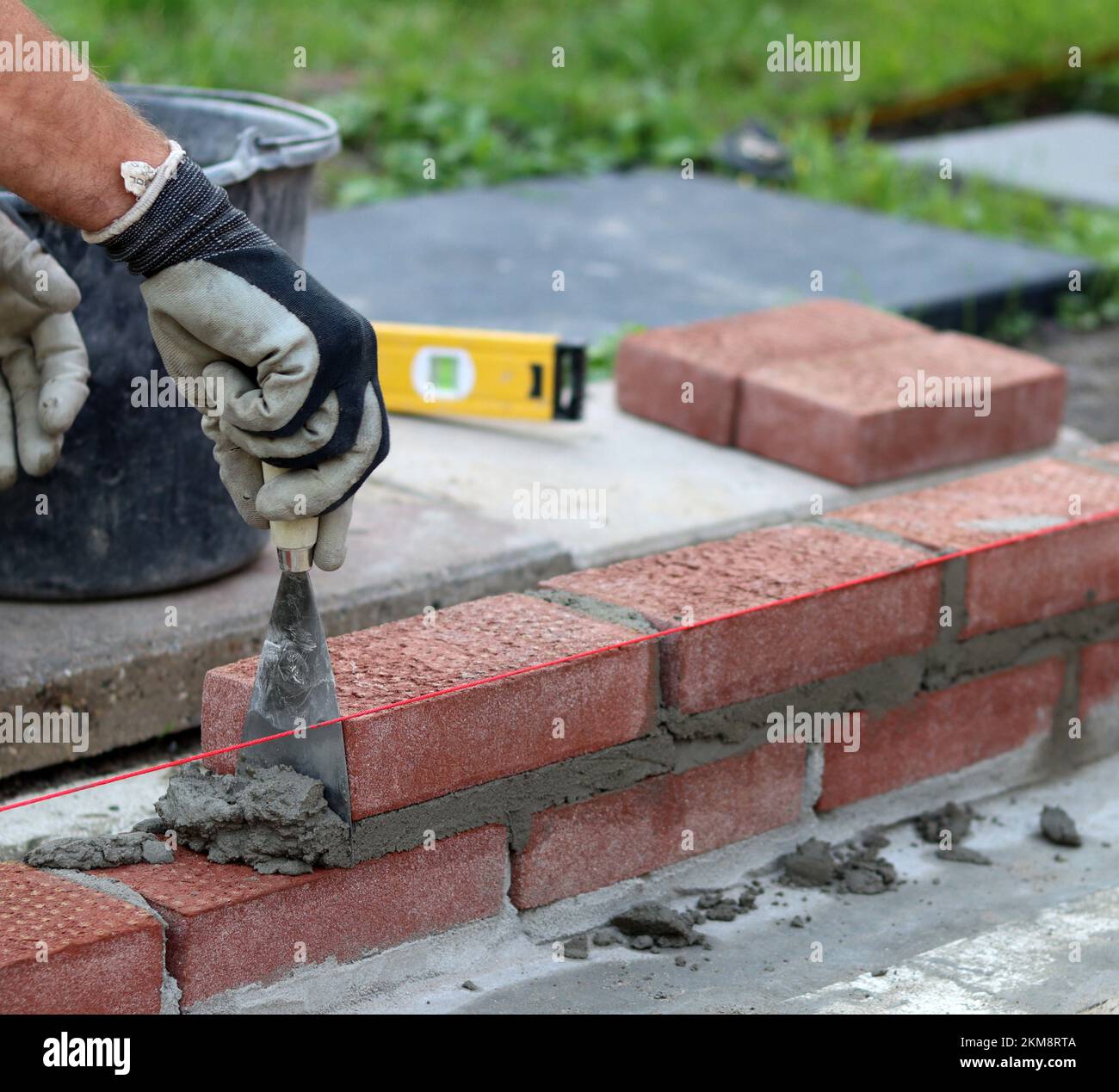 Bauarbeiten im Gange. Männlicher Baumeister, der mit roten Ziegeln arbeitet. Nahaufnahme der Mauerwand. Stockfoto