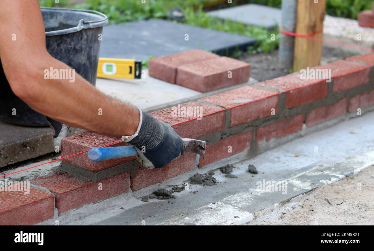 Bauarbeiten im Gange. Männlicher Baumeister, der mit roten Ziegeln arbeitet. Nahaufnahme der Mauerwand. Stockfoto