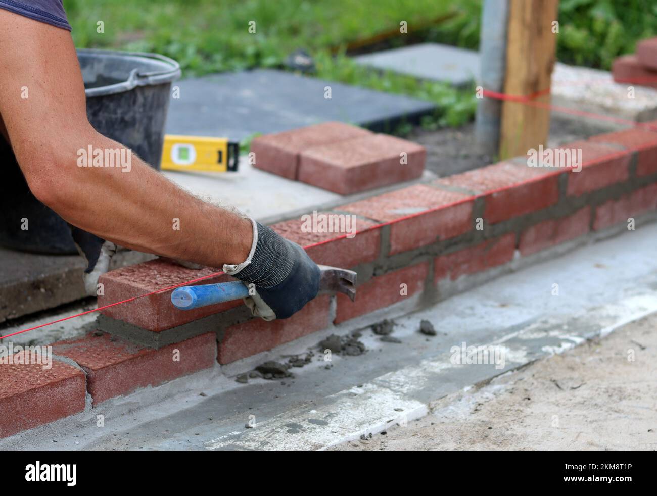 Bauarbeiten im Gange. Männlicher Baumeister, der mit roten Ziegeln arbeitet. Nahaufnahme der Mauerwand. Stockfoto