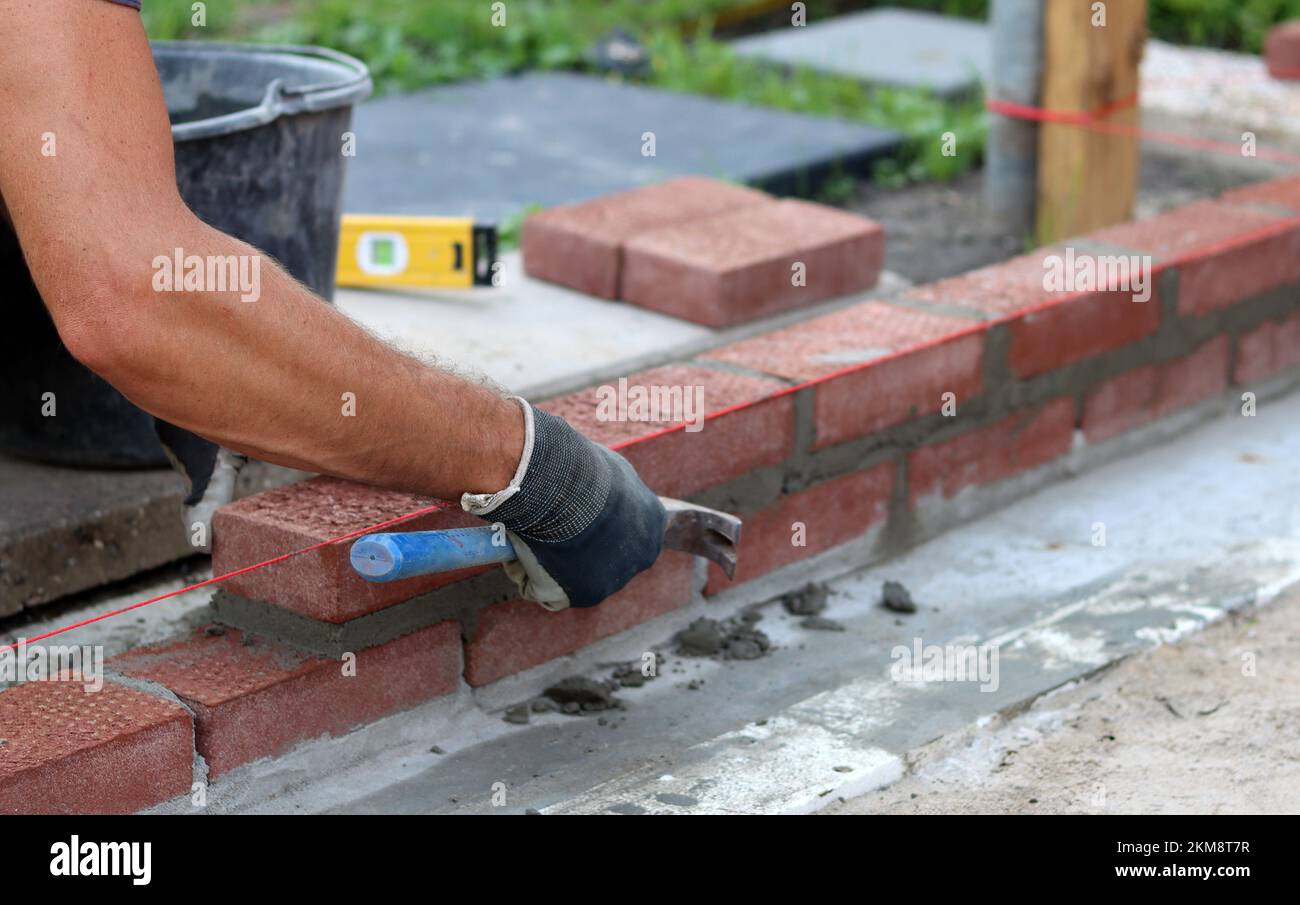 Bauarbeiten im Gange. Männlicher Baumeister, der mit roten Ziegeln arbeitet. Nahaufnahme der Mauerwand. Stockfoto