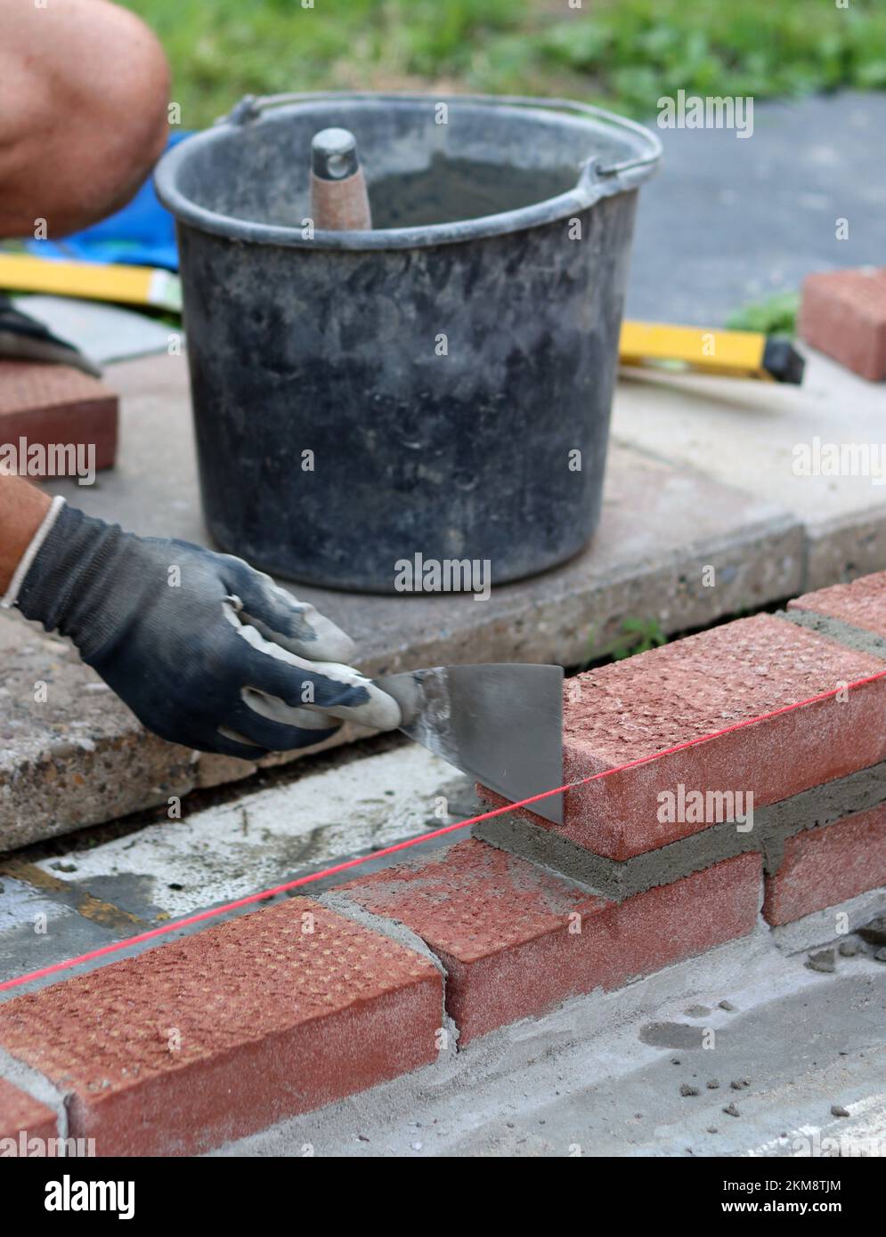 Bauarbeiten im Gange. Männlicher Baumeister, der mit roten Ziegeln arbeitet. Nahaufnahme der Mauerwand. Stockfoto