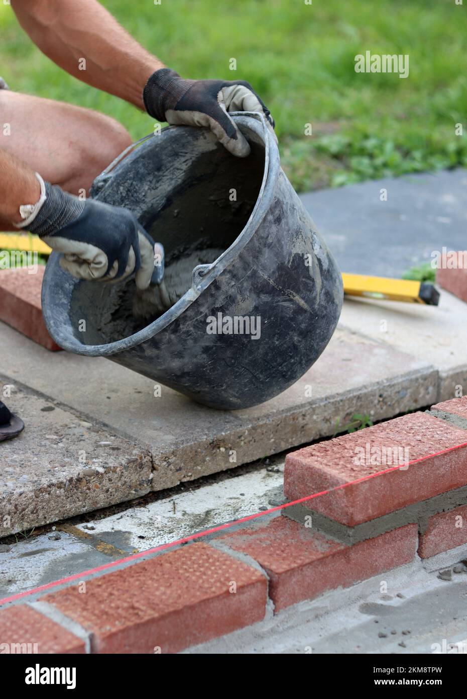 Bauarbeiten im Gange. Männlicher Baumeister, der mit roten Ziegeln arbeitet. Nahaufnahme der Mauerwand. Stockfoto