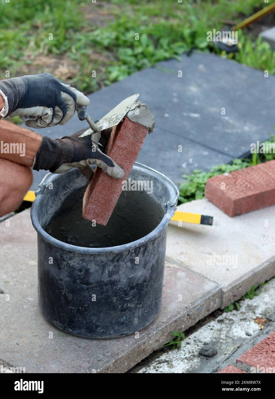Nahaufnahme von männlichen Händen mit rotem Ziegel. Baustellenkonzept. Professioneller Bau einer Ziegelwand. Stockfoto