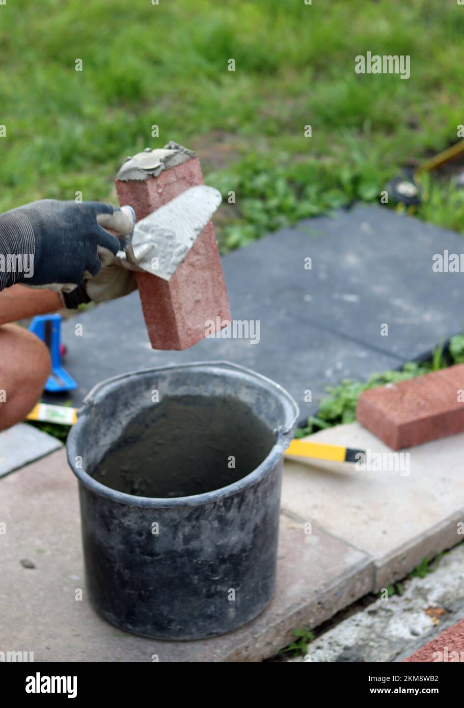 Nahaufnahme von männlichen Händen mit rotem Ziegel. Baustellenkonzept. Professioneller Bau einer Ziegelwand. Stockfoto