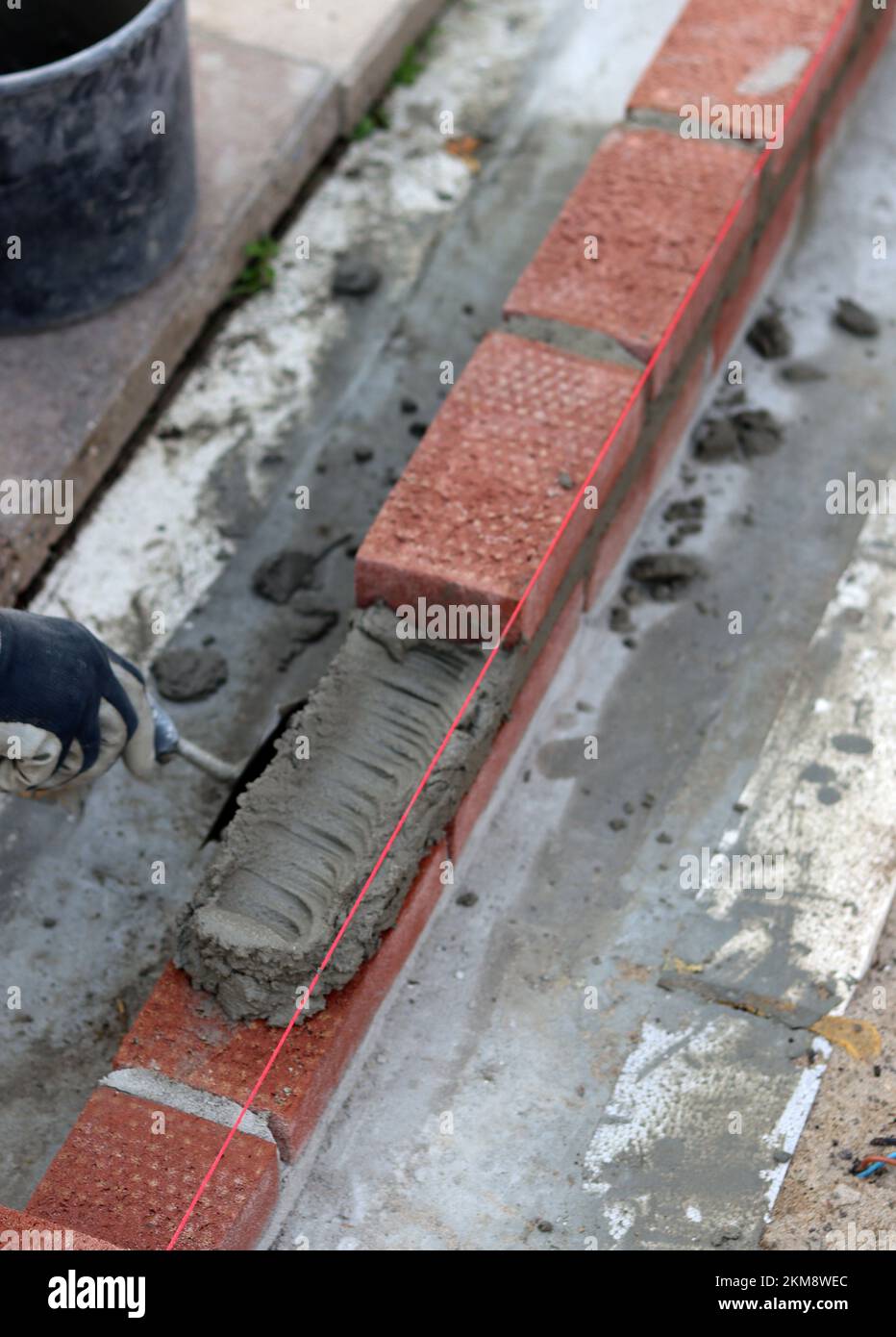 Bauarbeiten im Gange. Männlicher Baumeister, der mit roten Ziegeln arbeitet. Nahaufnahme der Mauerwand. Stockfoto