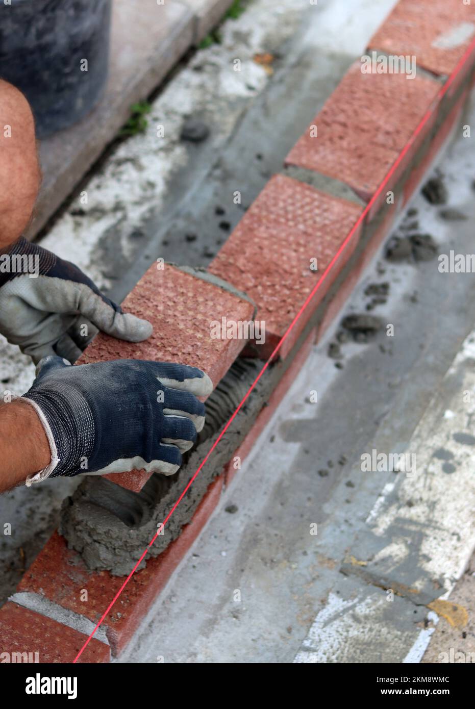 Nahaufnahme von männlichen Händen mit rotem Ziegel. Baustellenkonzept. Professioneller Bau einer Ziegelwand. Stockfoto