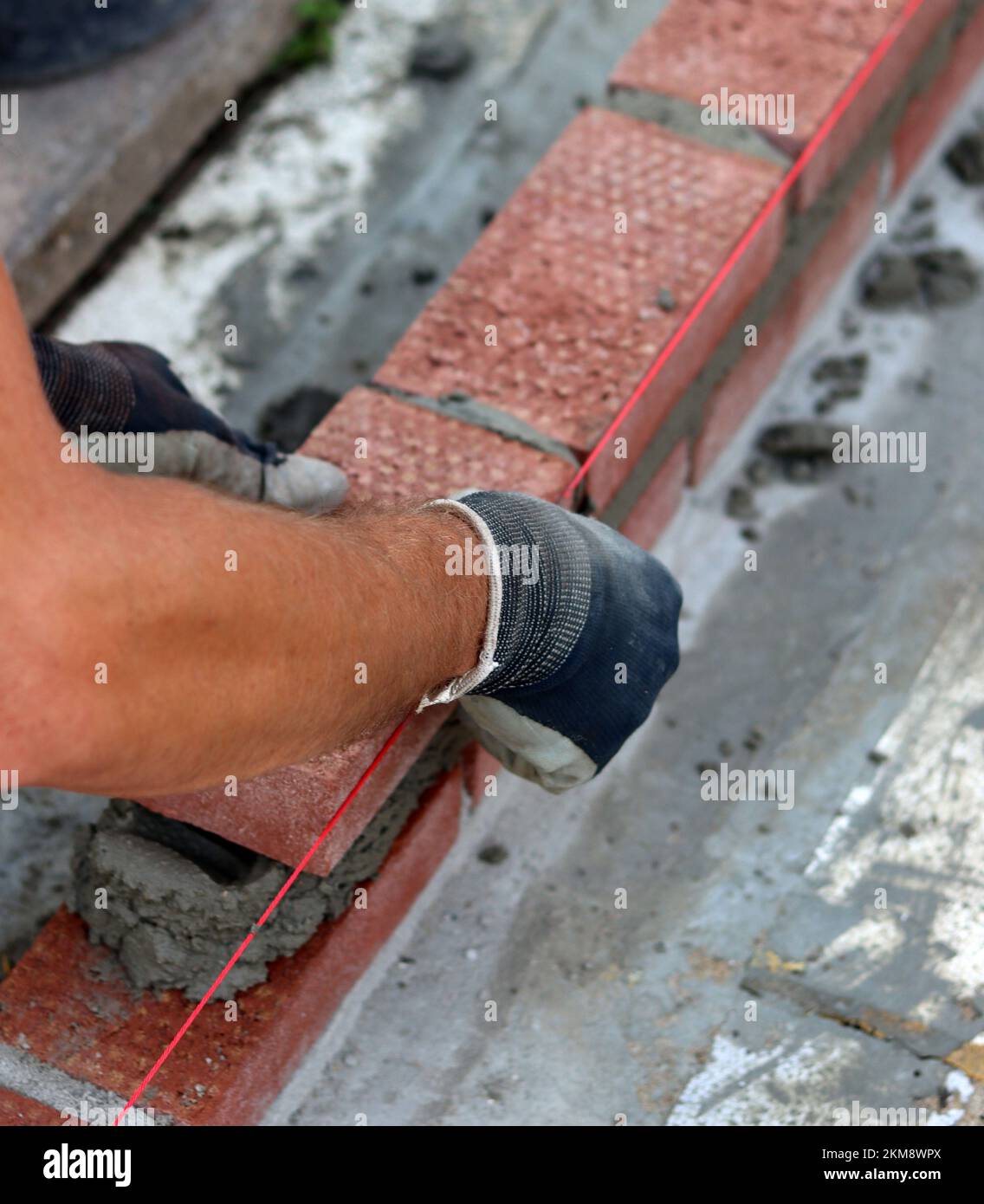 Bauarbeiten im Gange. Männlicher Baumeister, der mit roten Ziegeln arbeitet. Nahaufnahme der Mauerwand. Stockfoto