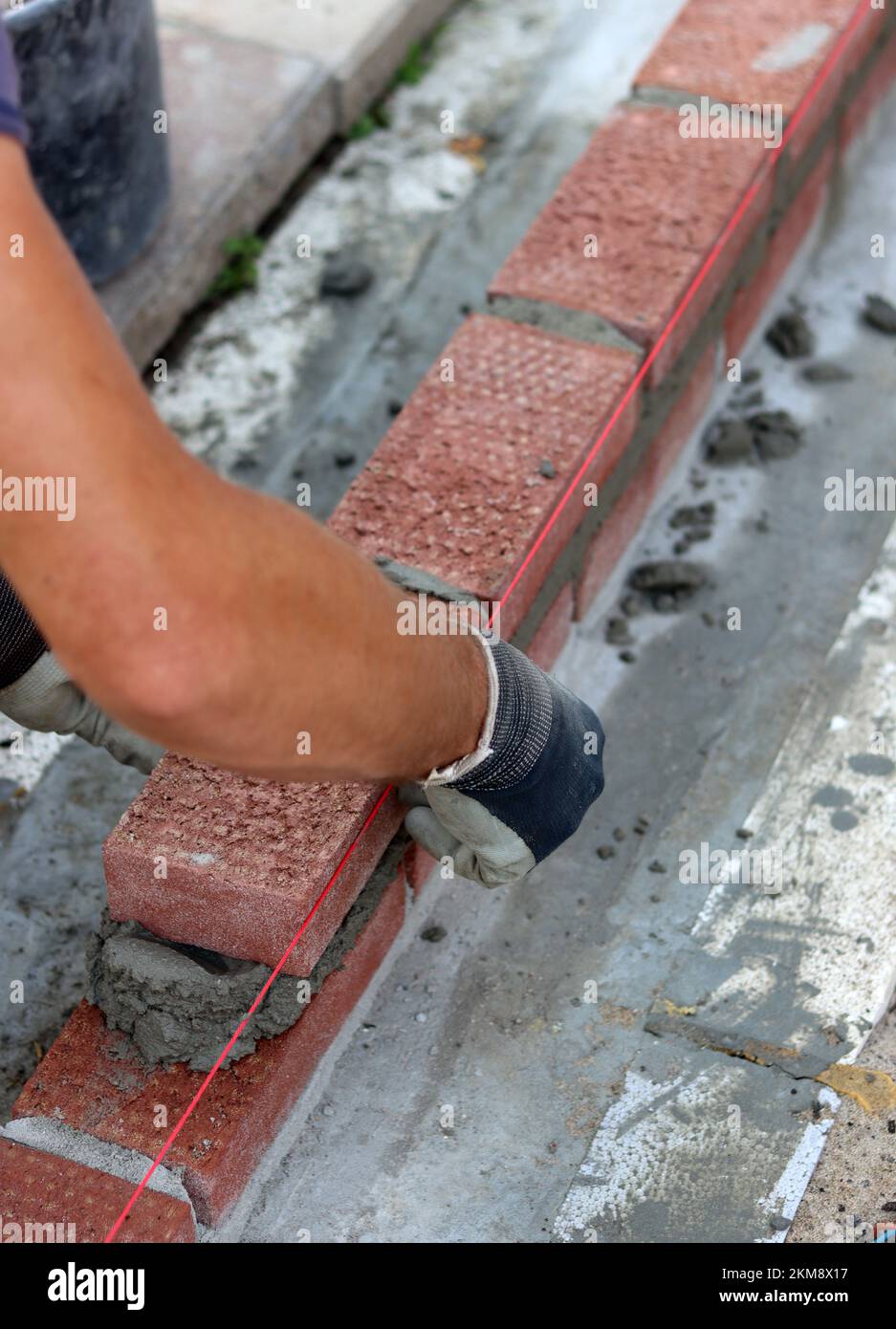 Bauarbeiten im Gange. Männlicher Baumeister, der mit roten Ziegeln arbeitet. Nahaufnahme der Mauerwand. Stockfoto