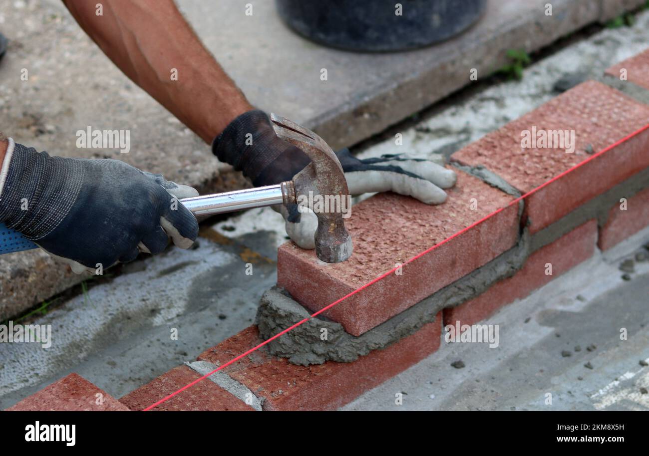 Nahaufnahme von männlichen Händen mit rotem Ziegel. Baustellenkonzept. Professioneller Bau einer Ziegelwand. Stockfoto