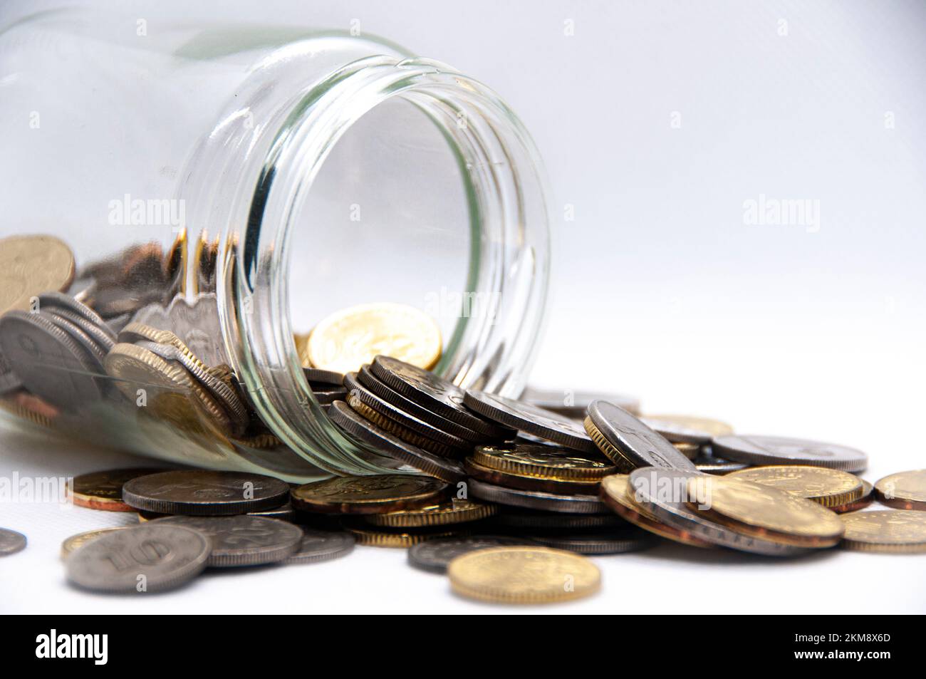 Nahaufnahme von Münzen in einem Glas auf weißem Hintergrund mit anpassbarem Platz für Text oder Ideen. Geschäfts- und Investitionskonzept. Stockfoto