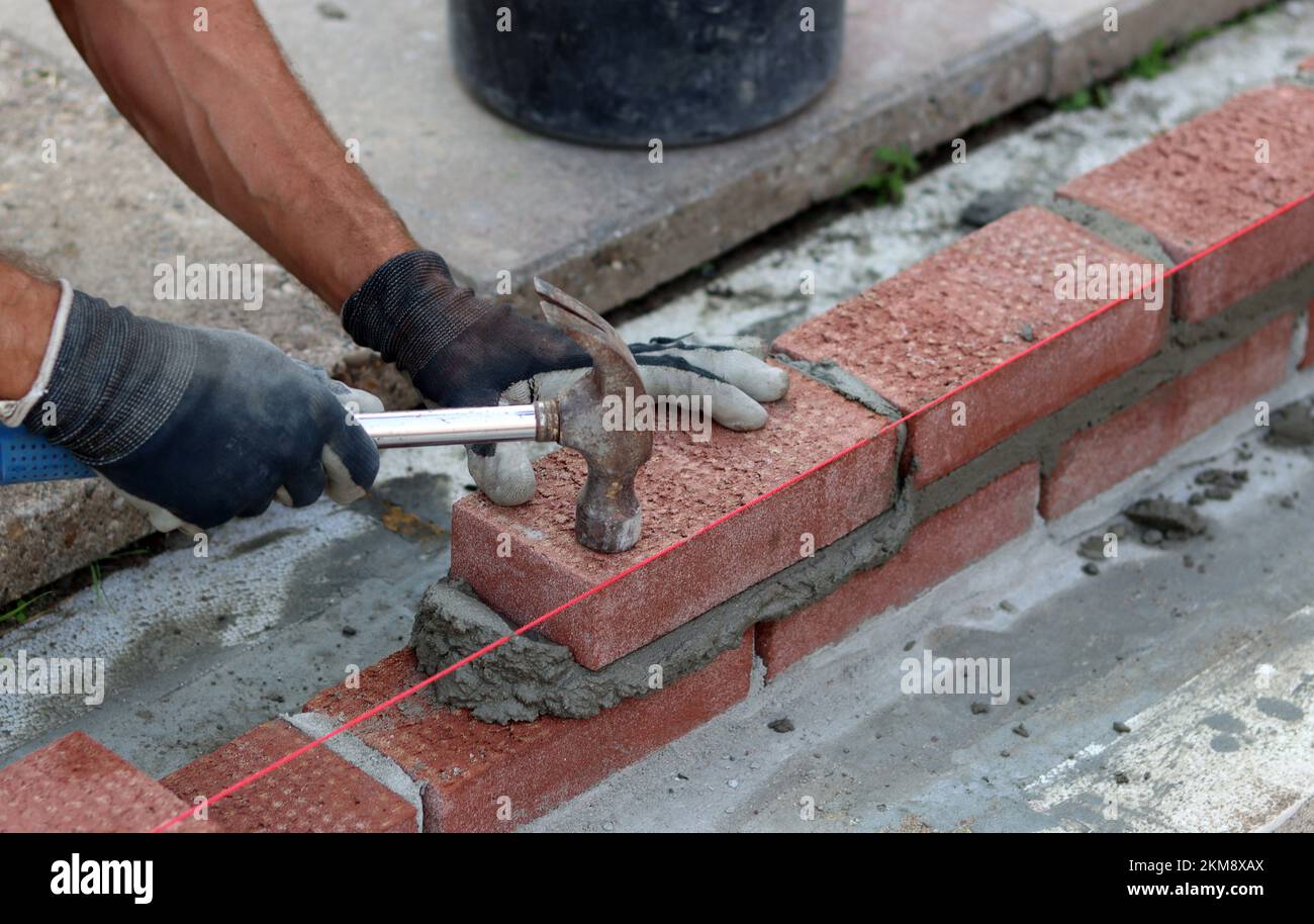 Bauarbeiten im Gange. Männlicher Baumeister, der mit roten Ziegeln arbeitet. Nahaufnahme der Mauerwand. Stockfoto