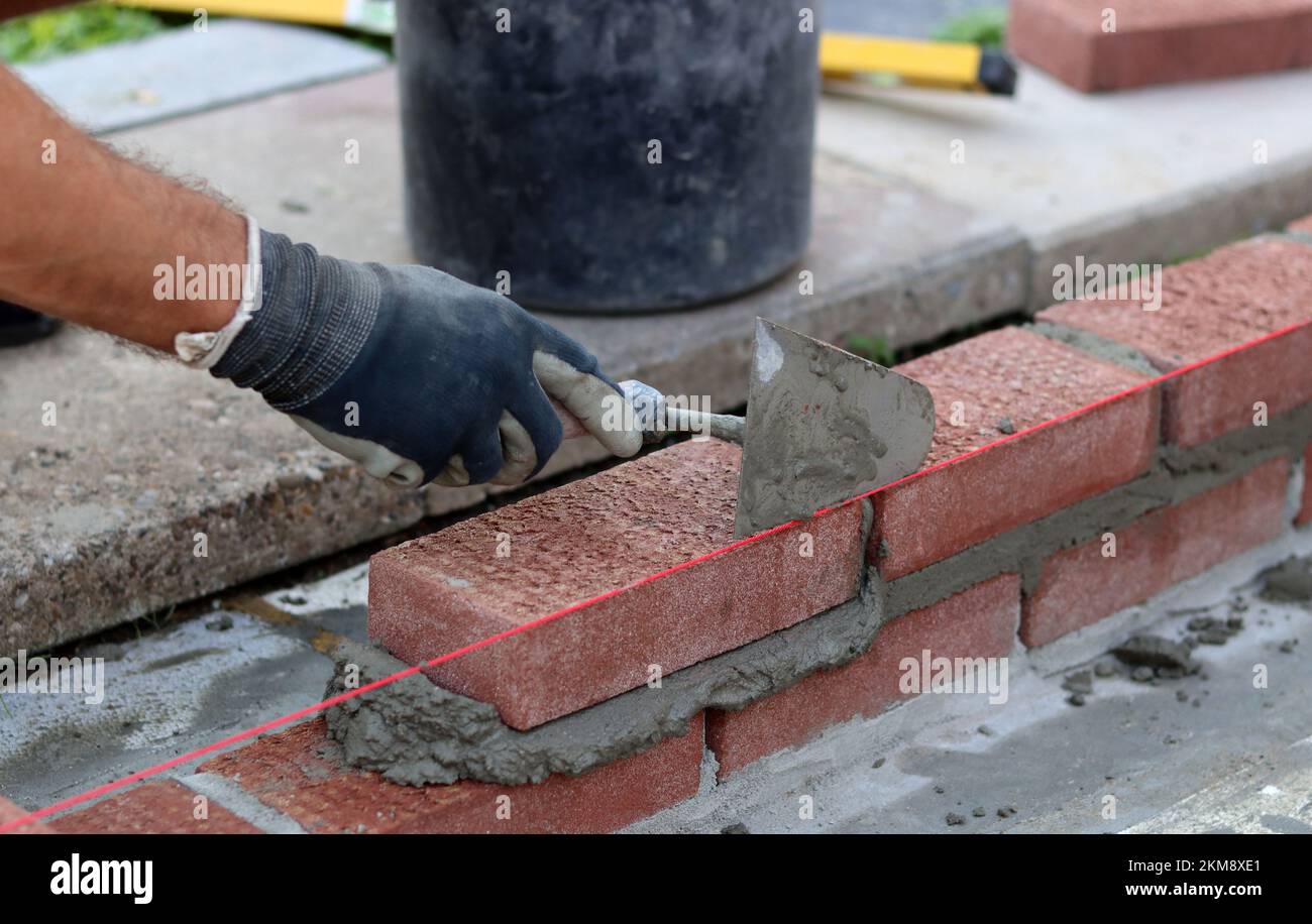 Bauarbeiten im Gange. Männlicher Baumeister, der mit roten Ziegeln arbeitet. Nahaufnahme der Mauerwand. Stockfoto