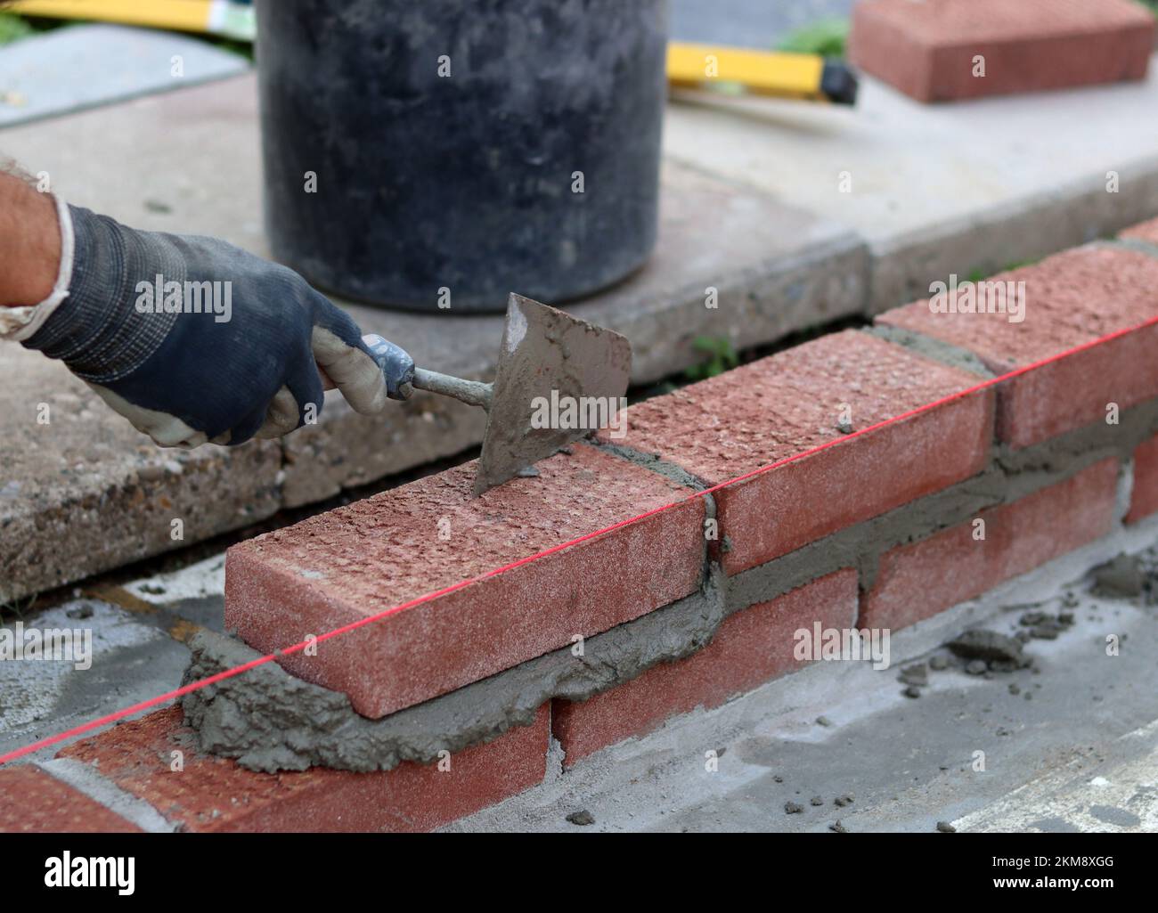Bauarbeiten im Gange. Männlicher Baumeister, der mit roten Ziegeln arbeitet. Nahaufnahme der Mauerwand. Stockfoto