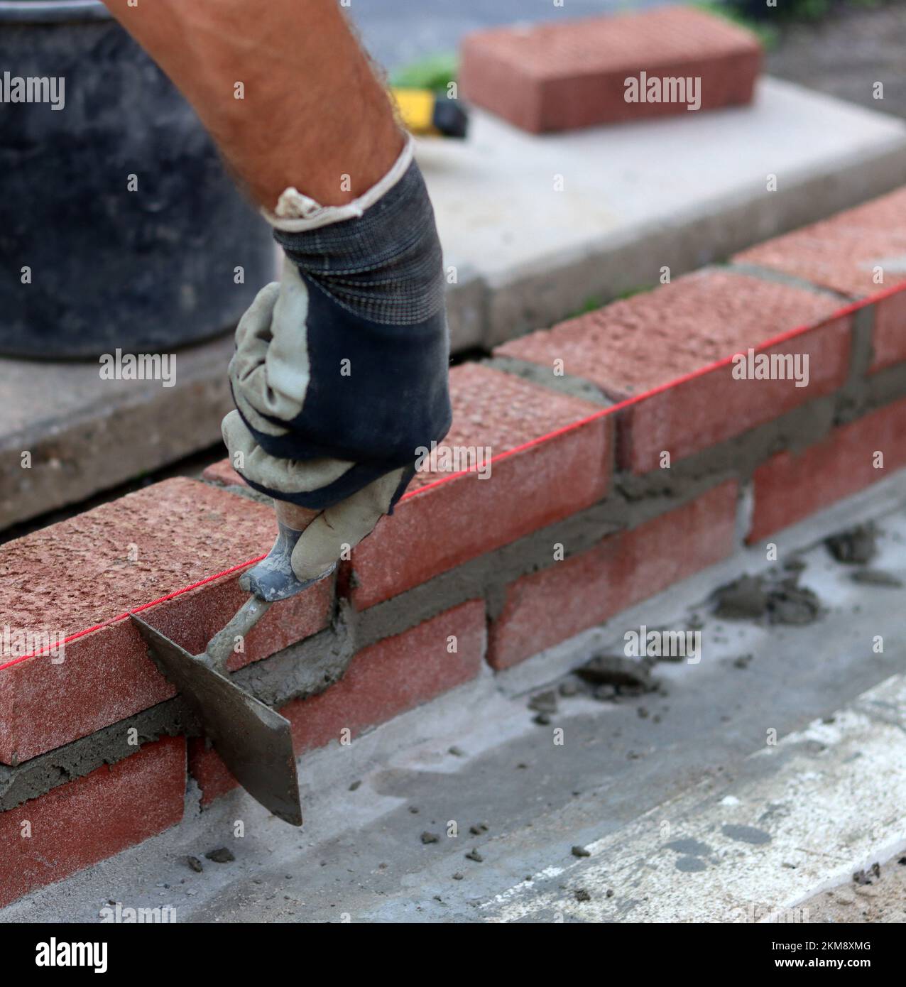 Bauarbeiten im Gange. Männlicher Baumeister, der mit roten Ziegeln arbeitet. Nahaufnahme der Mauerwand. Stockfoto