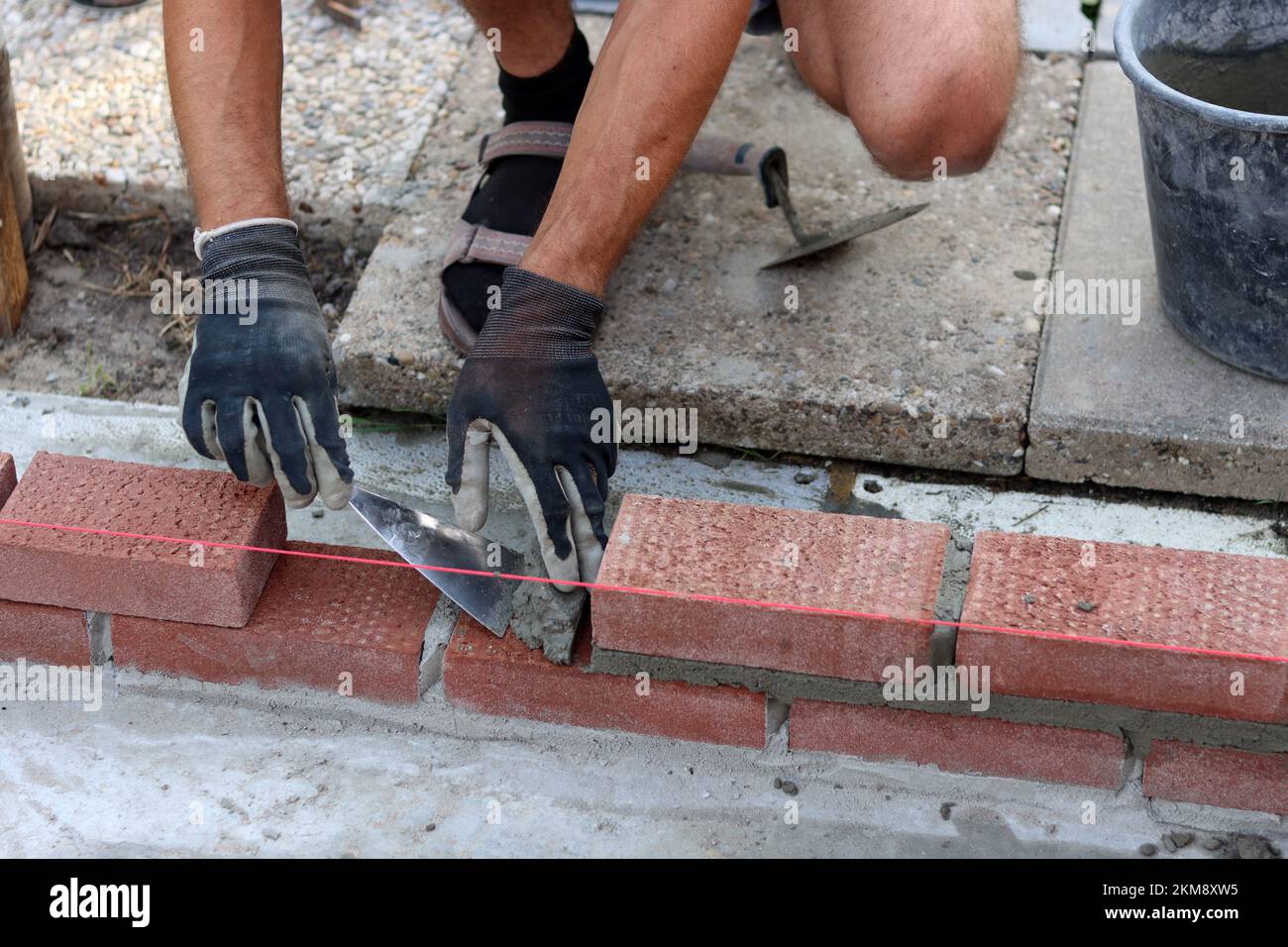 Bauarbeiten im Gange. Männlicher Baumeister, der mit roten Ziegeln arbeitet. Nahaufnahme der Mauerwand. Stockfoto