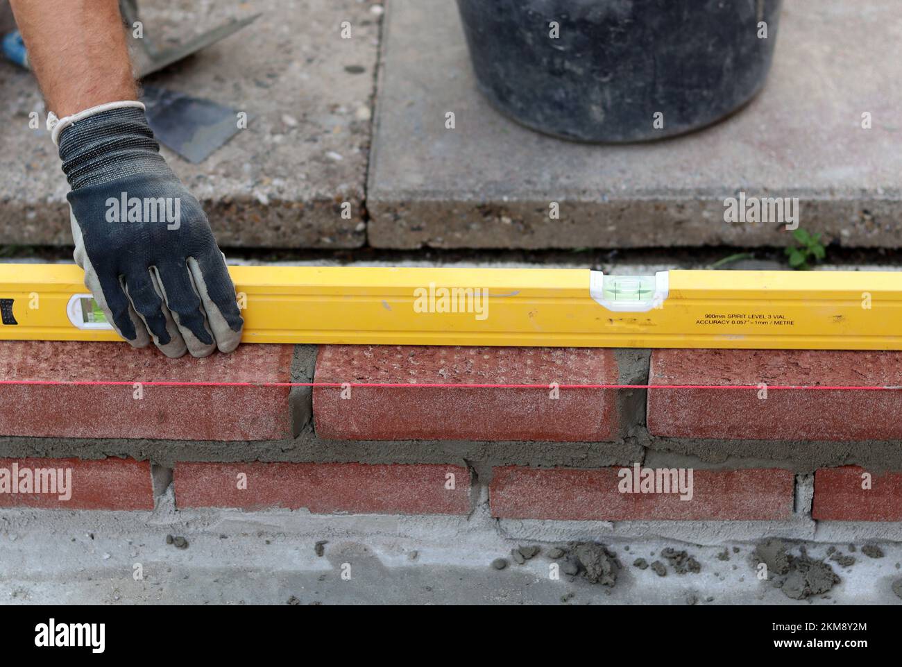 Eine Mauer aus roten Ziegeln zu bauen. Männliche Hände halten Maurerkelle und Nivelliermessgerät. Mauerwerk im Detail. Nahaufnahme der Baustelle. Stockfoto