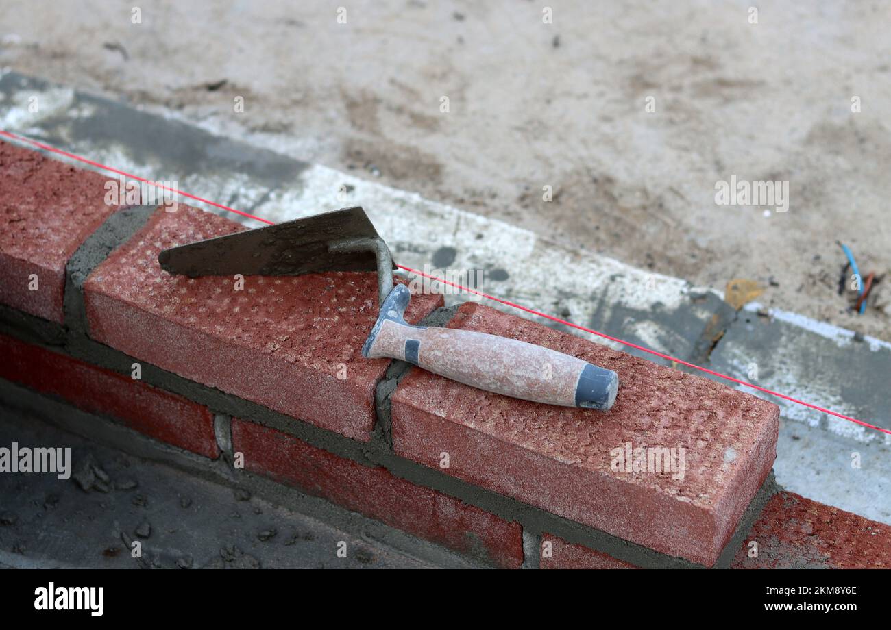 Maurerkelle an einer Wand. Nahaufnahme des Bauwerkzeugs. Baustelle. Stockfoto