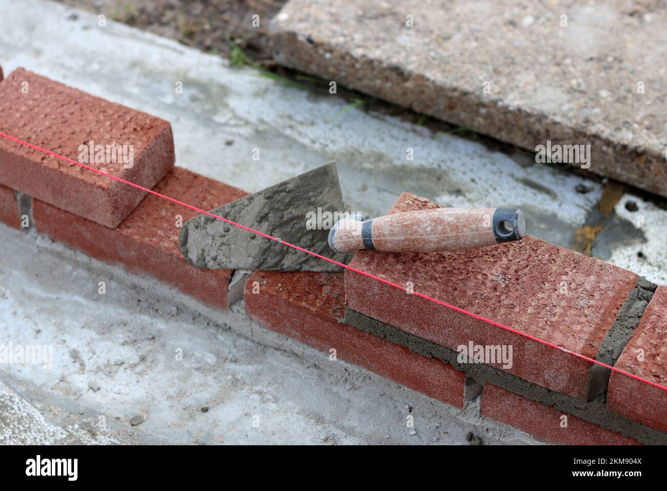 Maurerkelle an einer Wand. Nahaufnahme des Bauwerkzeugs. Baustelle. Stockfoto