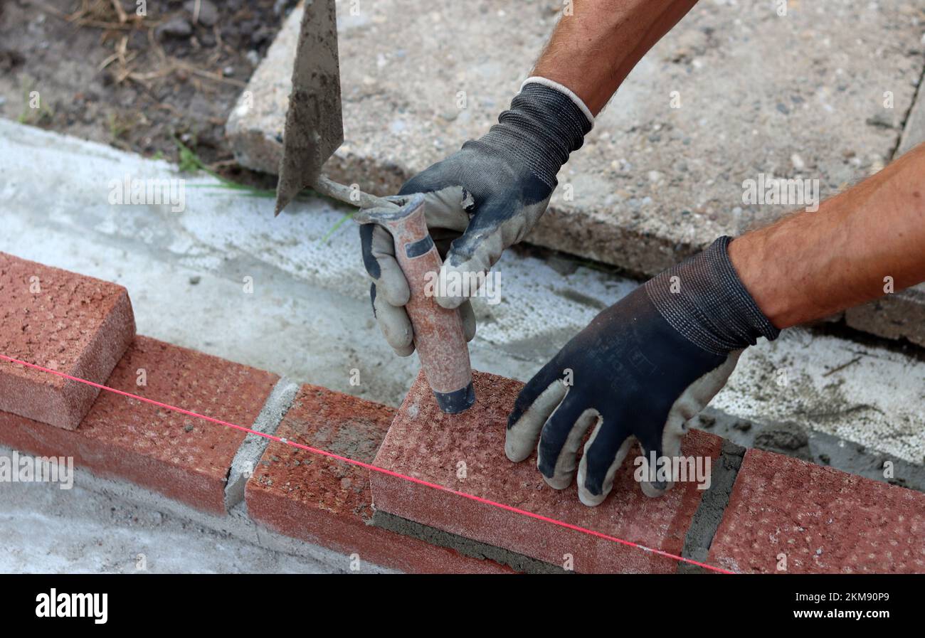 Nahaufnahme von männlichen Händen mit rotem Ziegel. Baustellenkonzept. Professioneller Bau einer Ziegelwand. Stockfoto