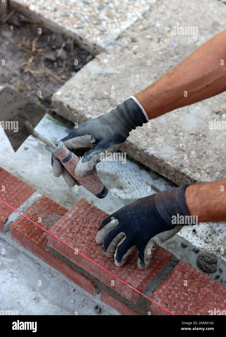 Bauarbeiten im Gange. Männlicher Baumeister, der mit roten Ziegeln arbeitet. Nahaufnahme der Mauerwand. Stockfoto