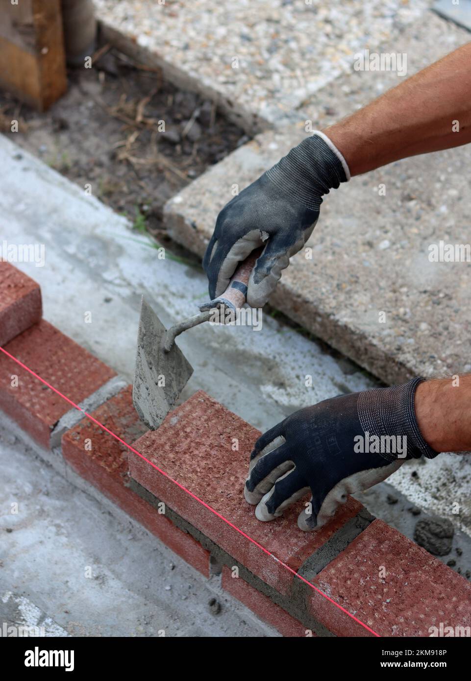 Nahaufnahme von männlichen Händen mit rotem Ziegel. Baustellenkonzept. Professioneller Bau einer Ziegelwand. Stockfoto
