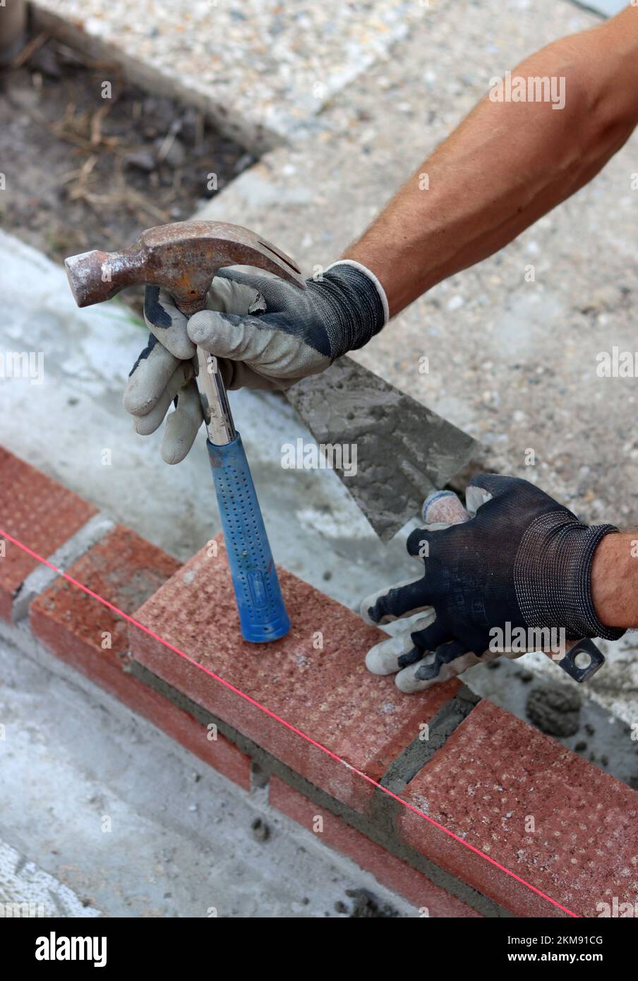 Bauarbeiten im Gange. Männlicher Baumeister, der mit roten Ziegeln arbeitet. Nahaufnahme der Mauerwand. Stockfoto