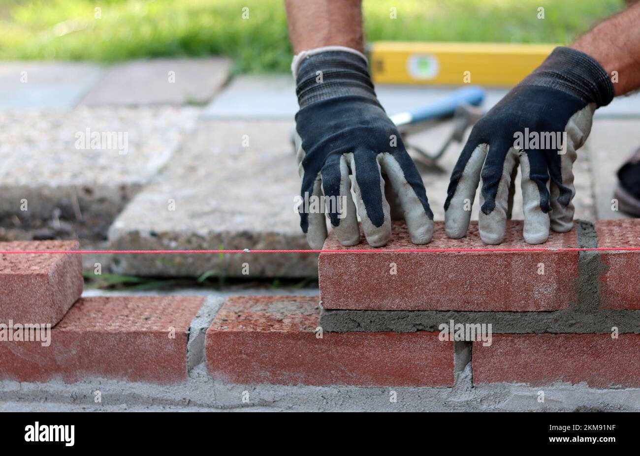 Eine Mauer aus roten Ziegeln zu bauen. Männliche Hände halten Maurerkelle und Nivelliermessgerät. Mauerwerk im Detail. Nahaufnahme der Baustelle. Stockfoto