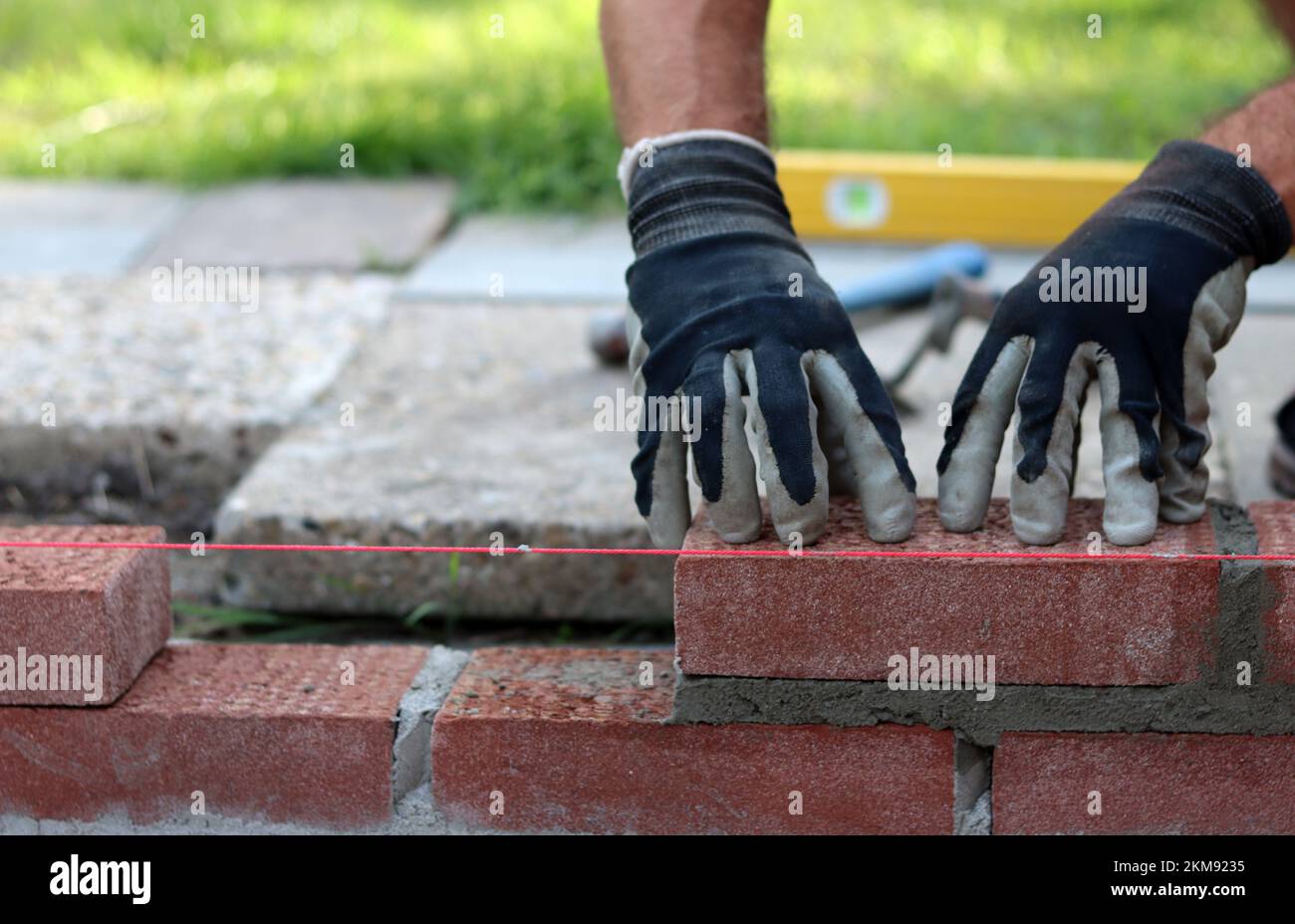 Eine Mauer aus roten Ziegeln zu bauen. Männliche Hände halten Maurerkelle und Nivelliermessgerät. Mauerwerk im Detail. Nahaufnahme der Baustelle. Stockfoto