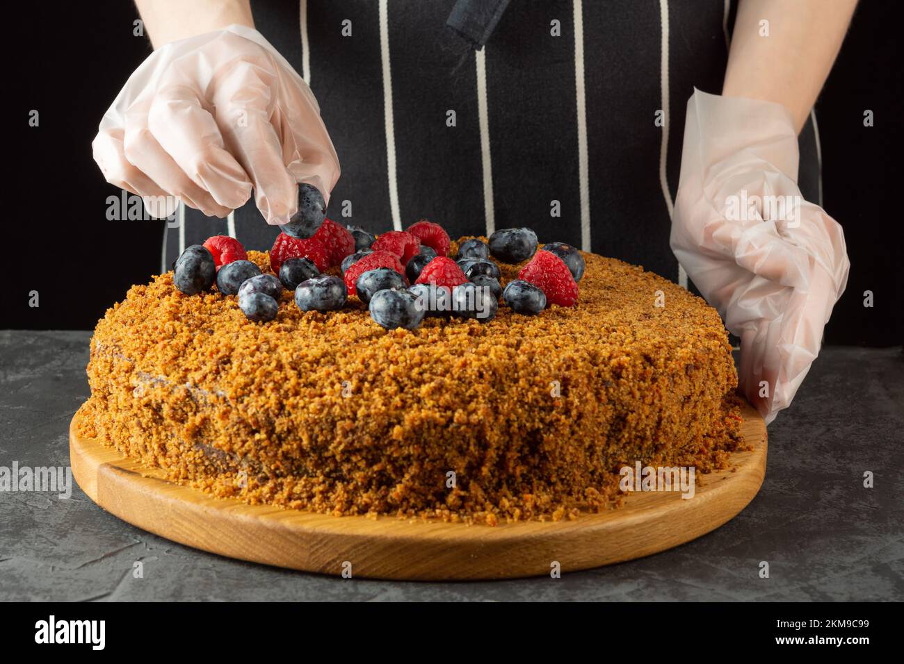 Eine Chefköchin schmückt einen hausgemachten Karottenkuchen mit frischen Beeren auf dunklem Hintergrund. Selektiver Fokus Stockfoto